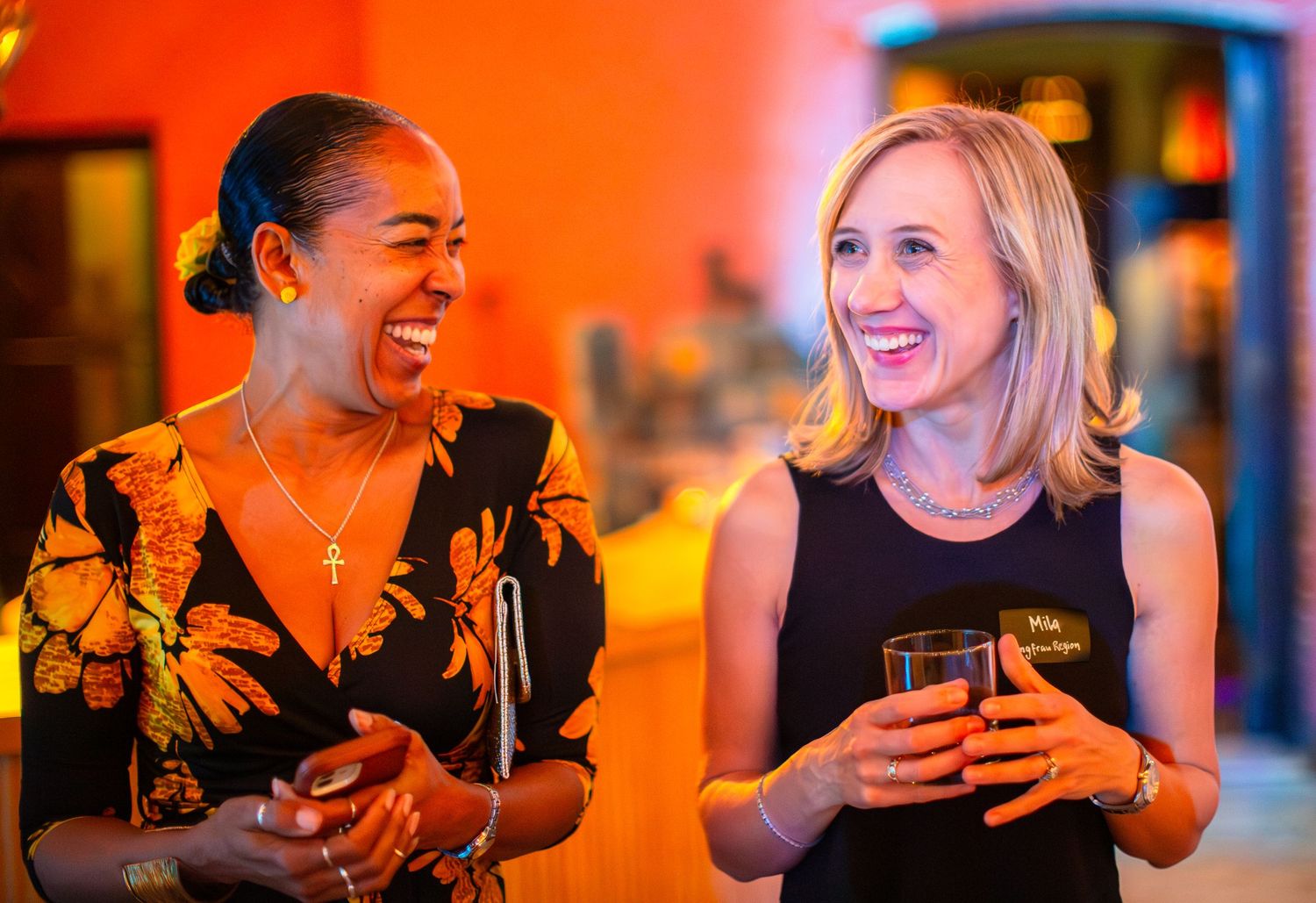 Two friends enjoying drinks and conversation at an evening social event.