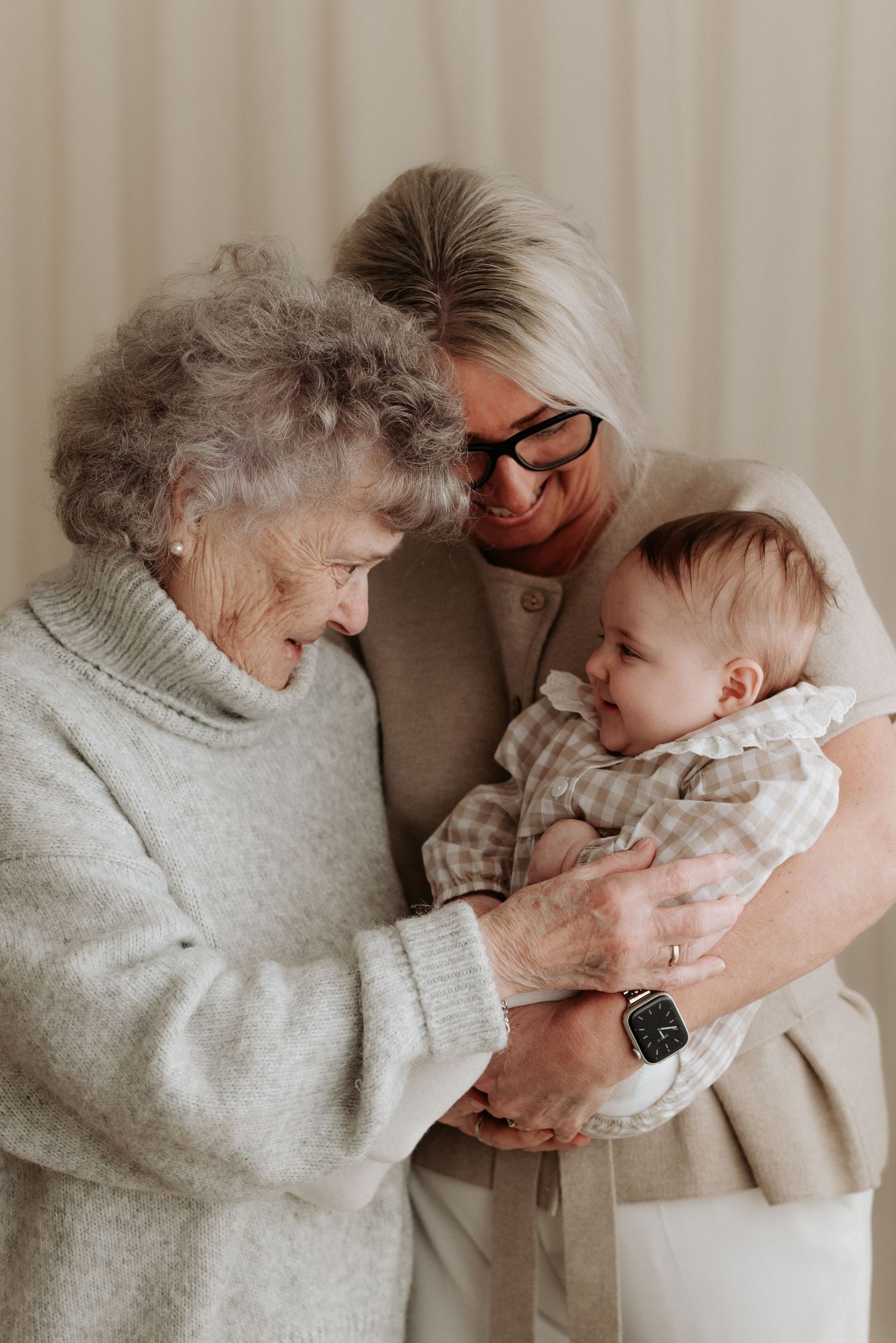 Elderly great-grandmother and grandmother smiling at a newborn baby held in their arms.