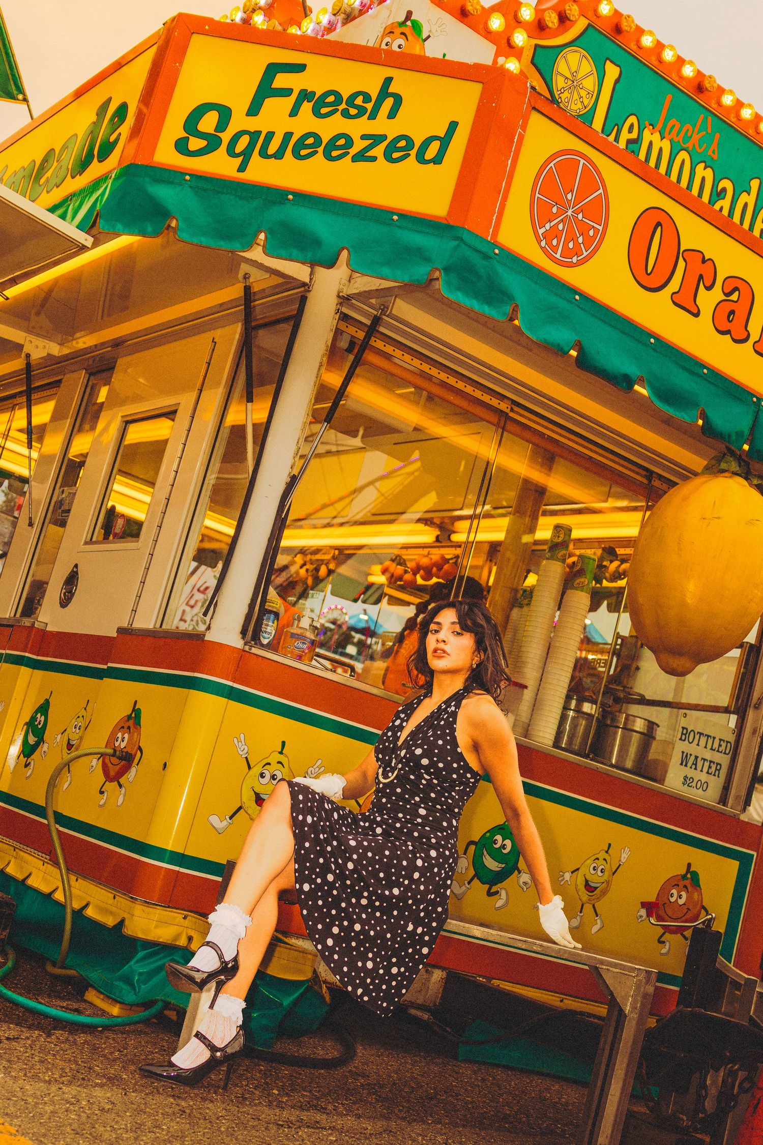 Woman in polka dot dress posing by a colorful fresh squeezed lemonade stand at a carnival fair.