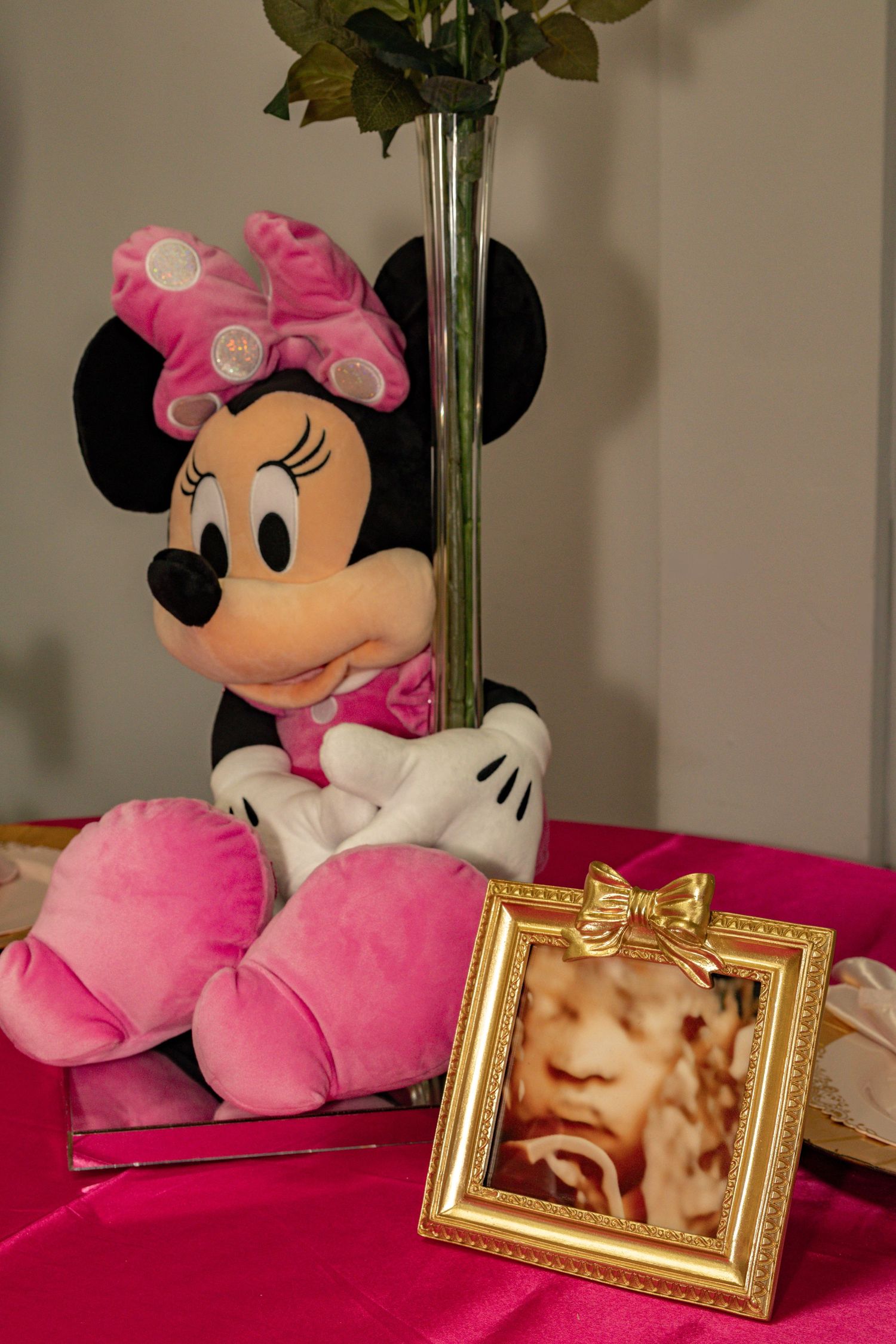 Pink Minnie Mouse plush toy beside a gold-framed ultrasound photo on a pink satin tablecloth.