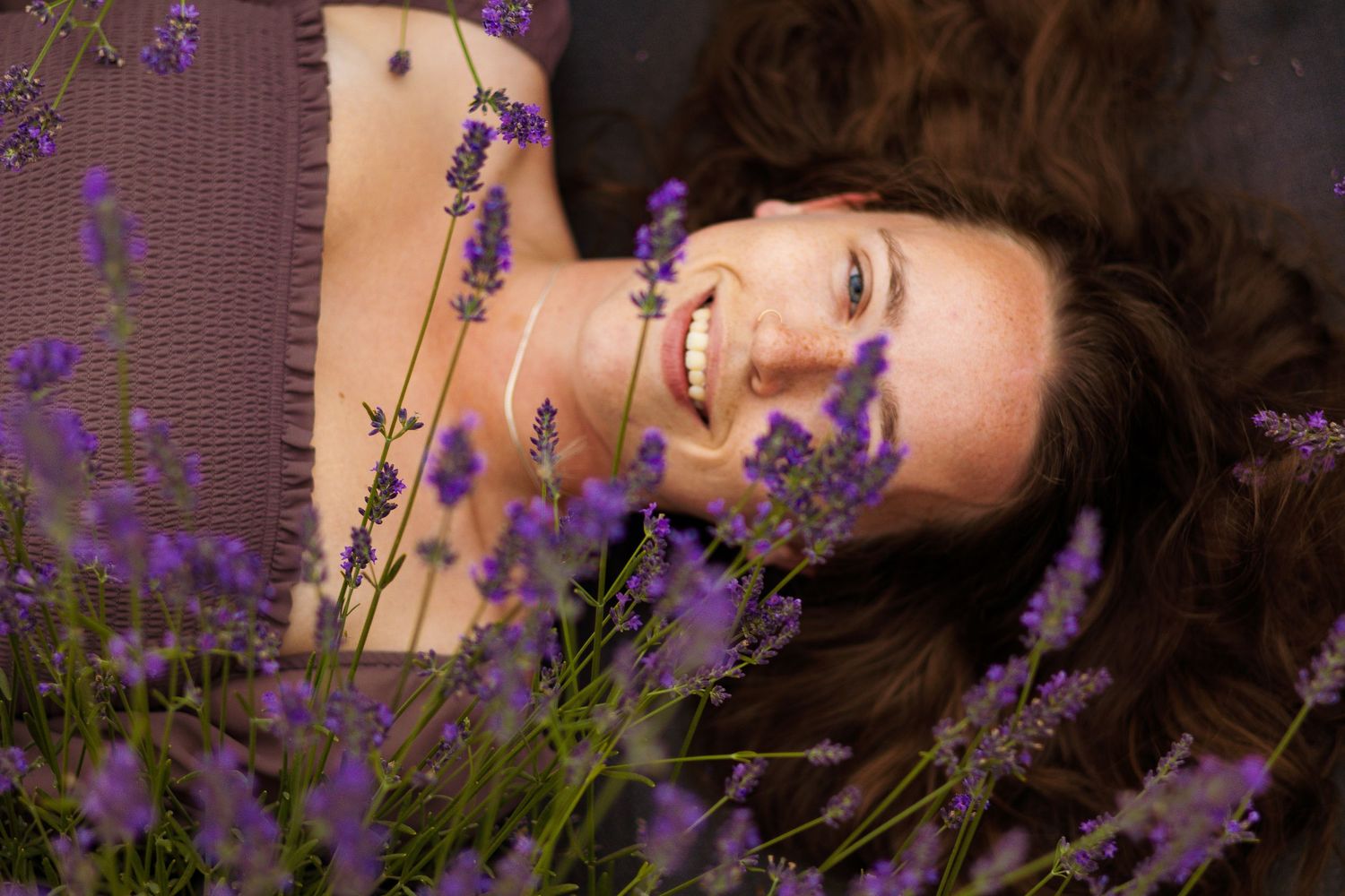 Close-up portrait of someone lying among purple lavender flowers on a sunny day.