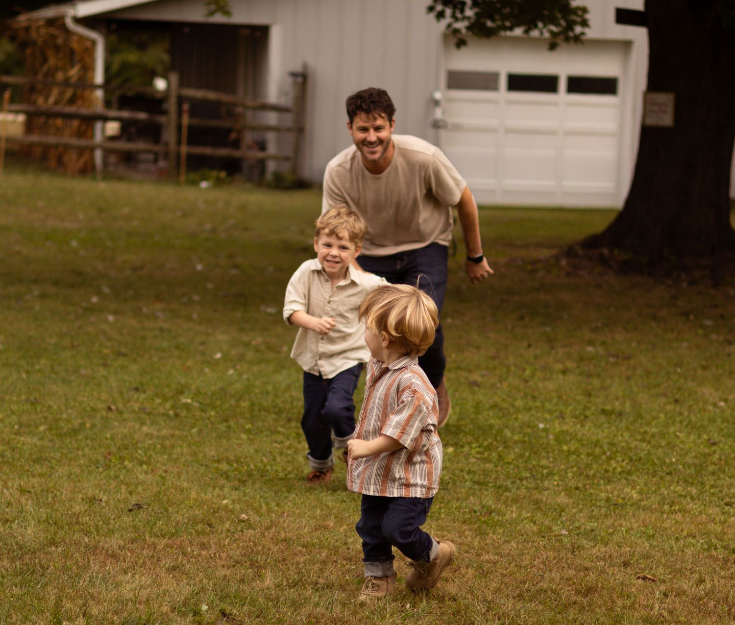 A playful chase scene unfolds on a grassy lawn near a garage.