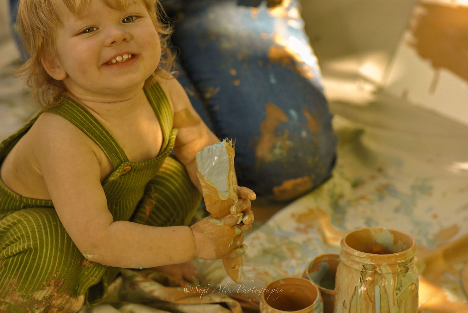 A small child in green overalls plays with art supplies on the floor.