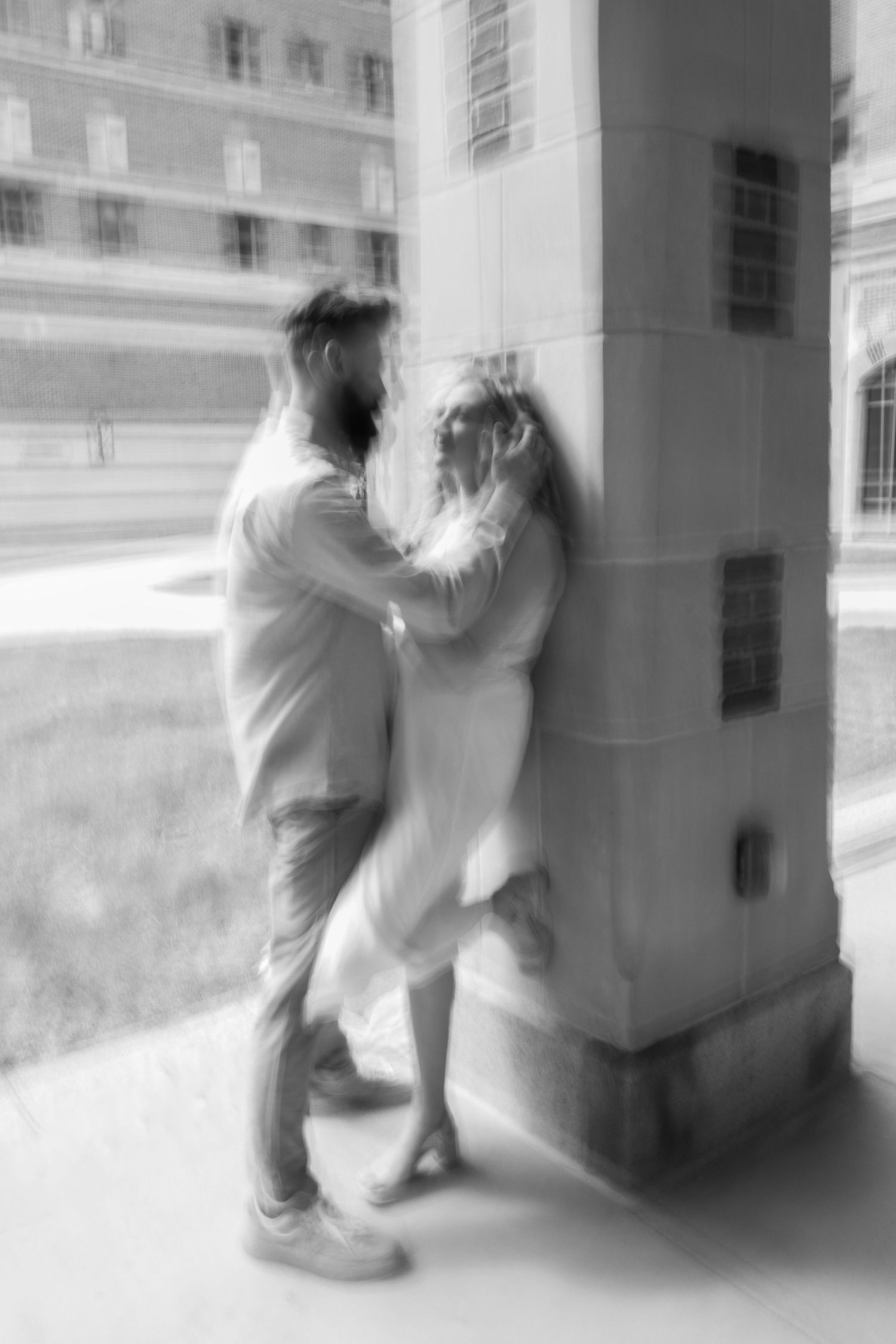 A romantic black and white photo of a couple embracing against a building column.