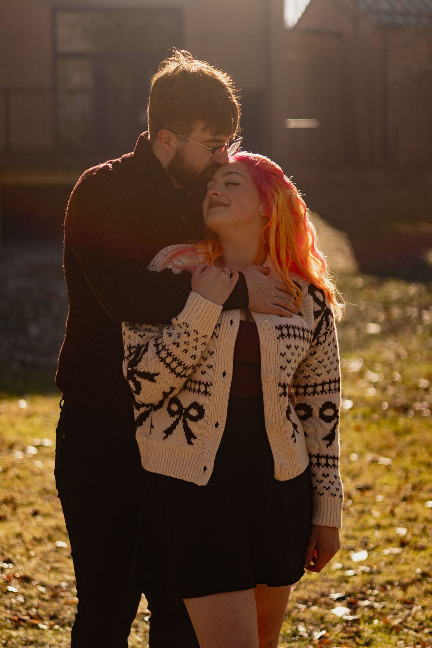 A romantic couple in matching winter sweaters embrace during golden hour on fallen autumn leaves.