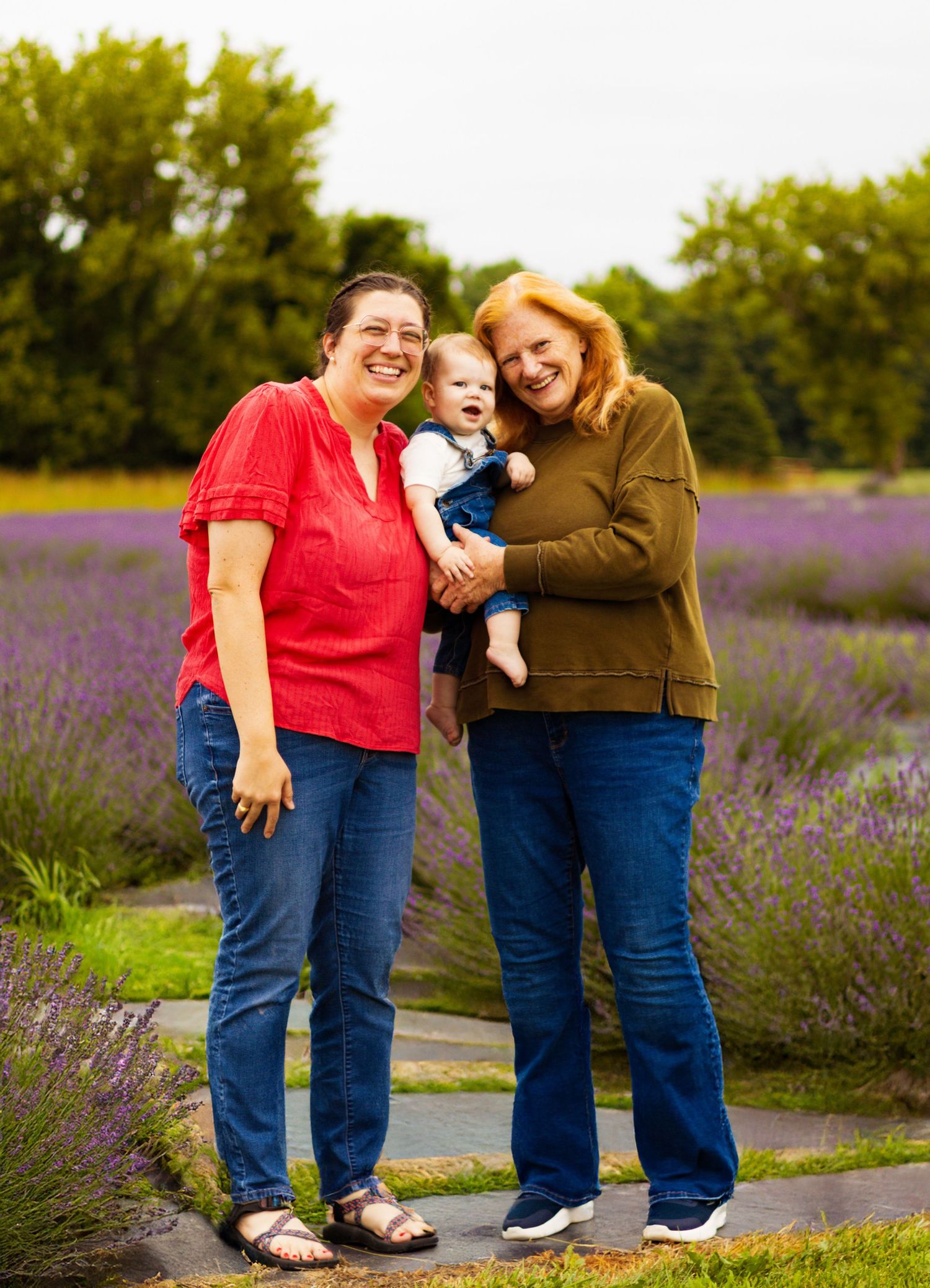 Three people pose casually together on a path through blooming lavender fields.