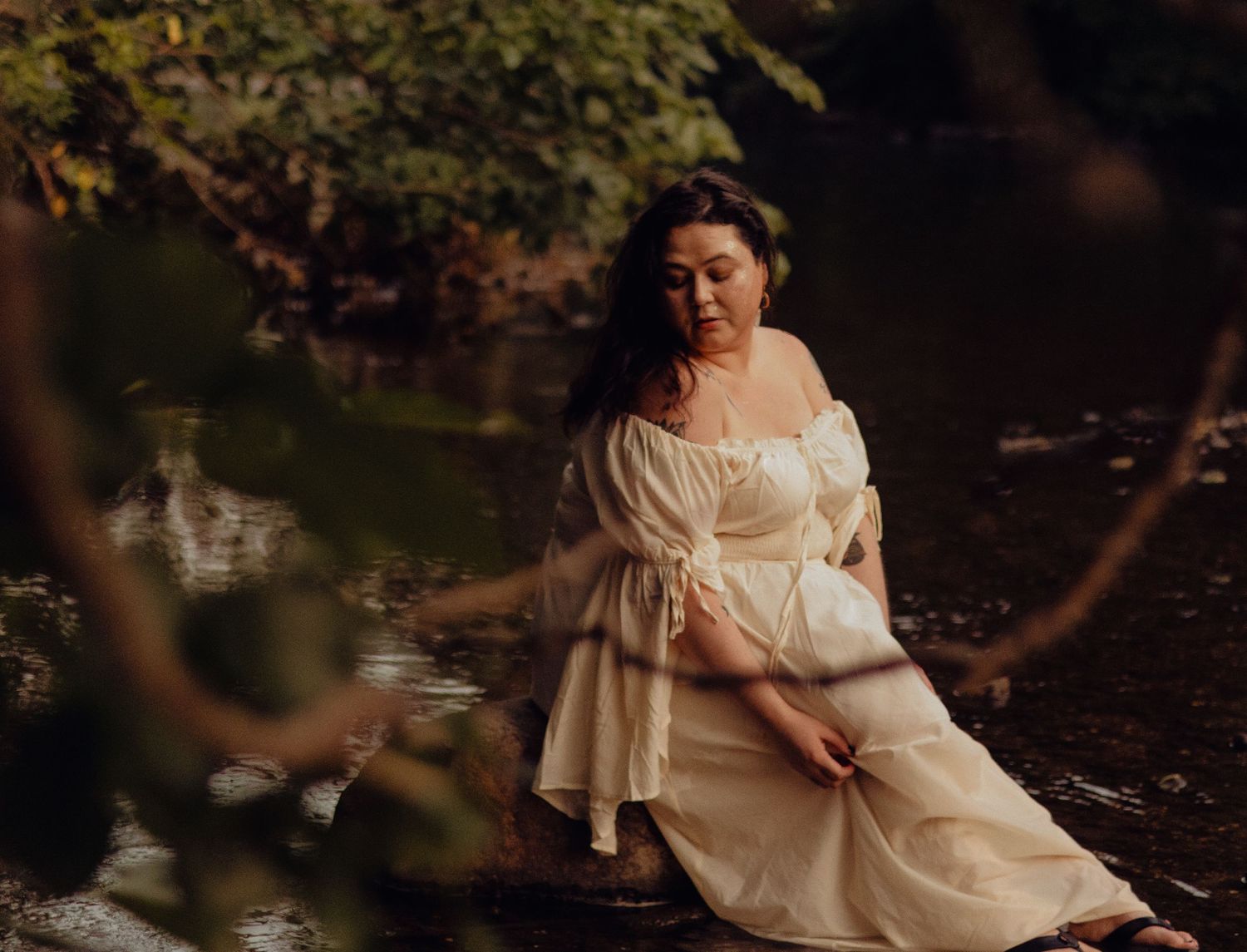 A flowing white dress creates ethereal movement against a dark natural backdrop.