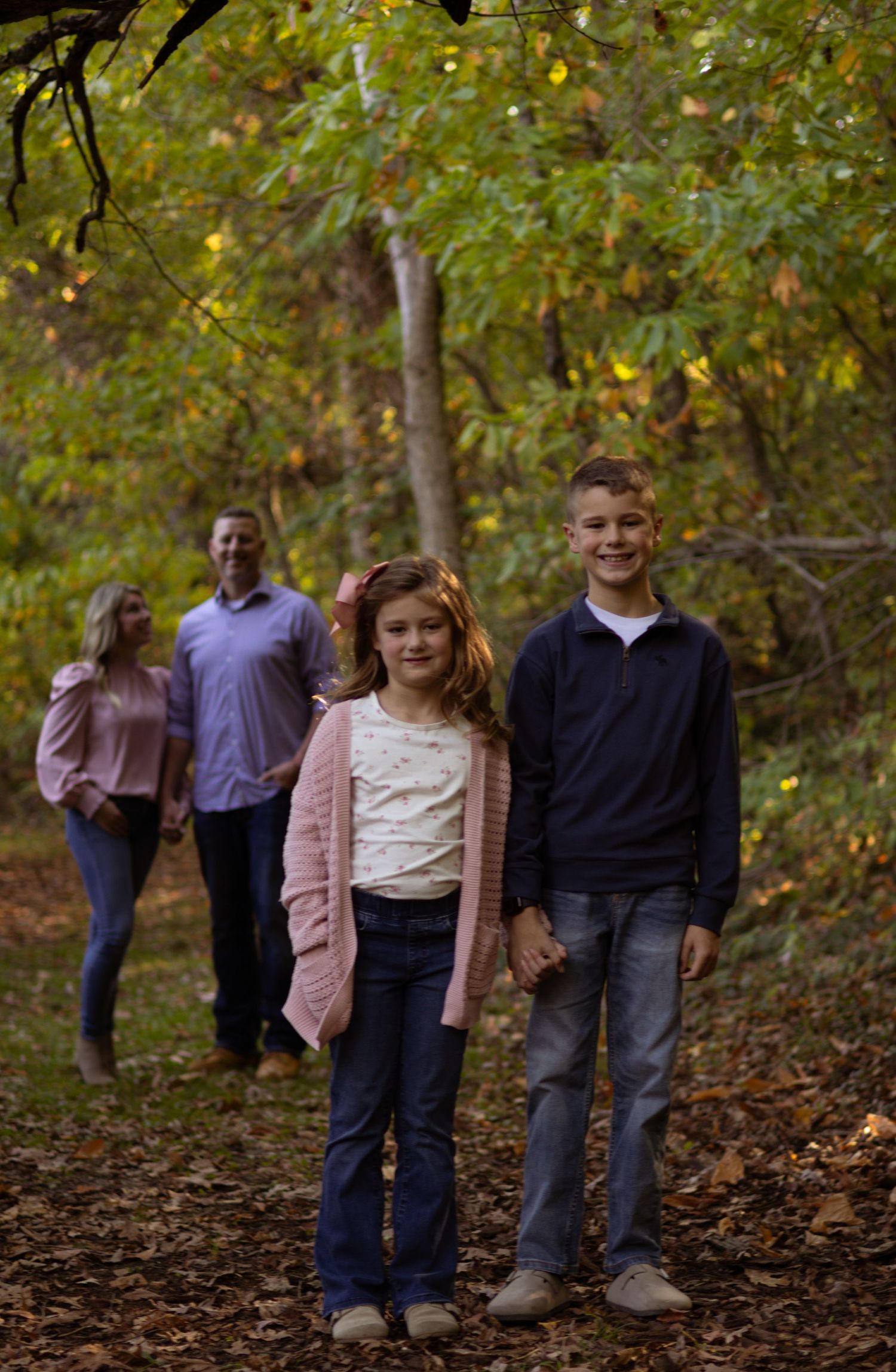 Family poses for portraits among autumn trees on a wooded trail.