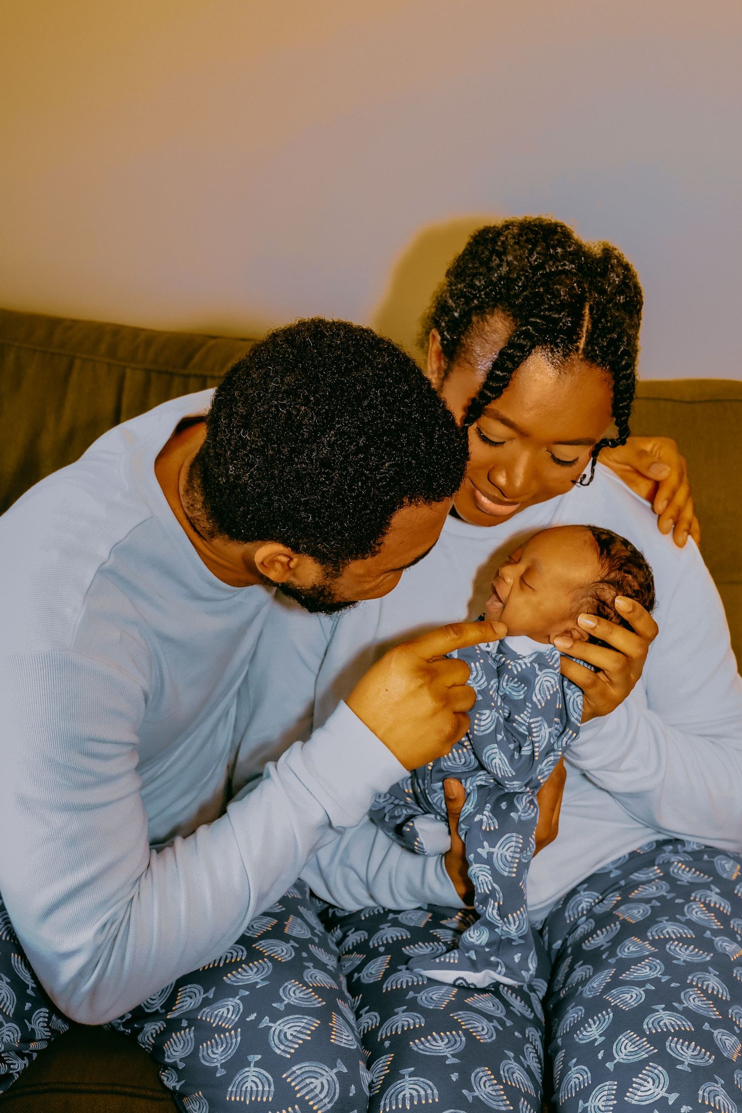 A couple in matching pajamas lovingly gazes at their newborn baby, sharing a tender family moment.