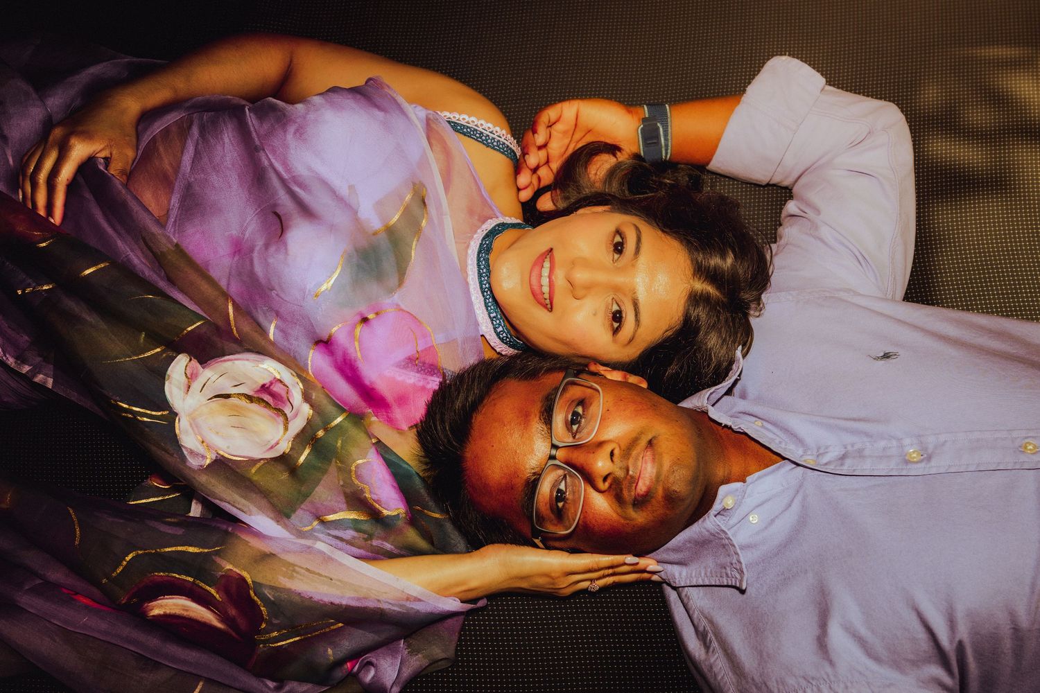 Couple lying down together with flowers, woman in purple dress and man in blue shirt, romantic portrait photography.