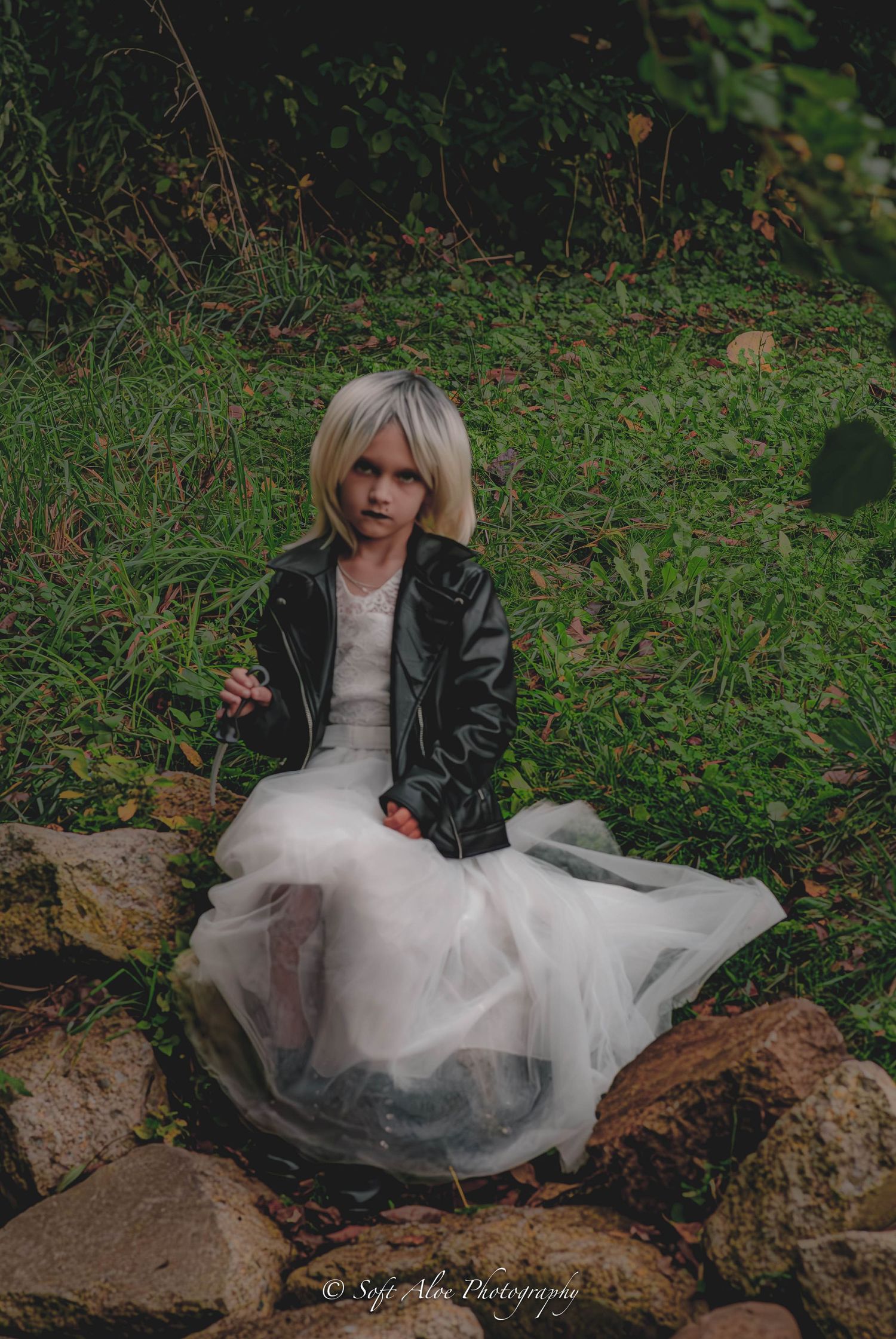 Dramatic outdoor photoshoot featuring a white tulle dress and leather jacket among rocks and foliage.