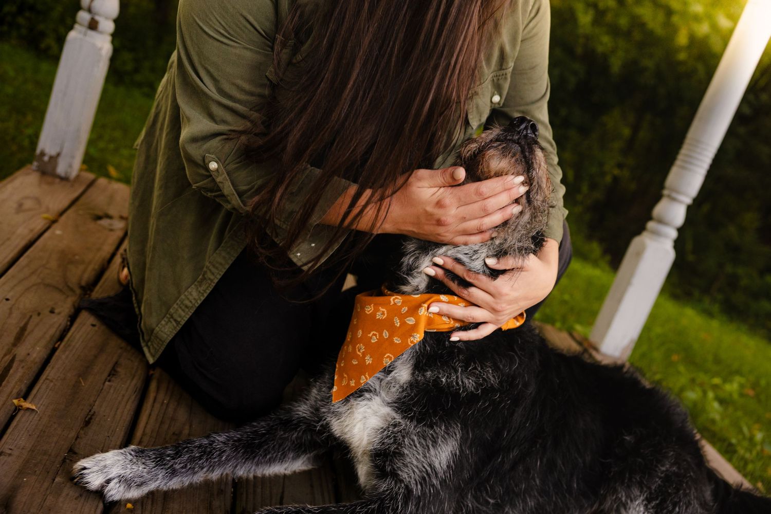 Woman sitting on wooden porch cuddling newborn baby while large black and white dog rests nearby.