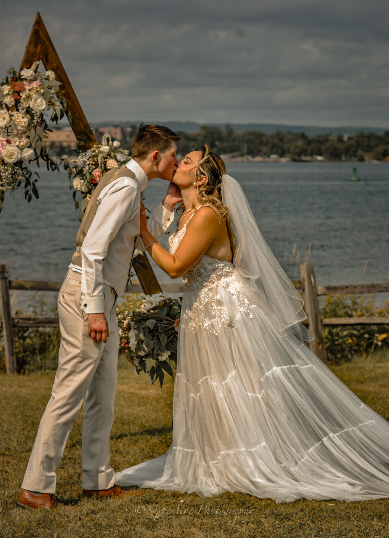 A romantic wedding couple shares a tender moment by a scenic waterfront with flowing white dress and veil details.