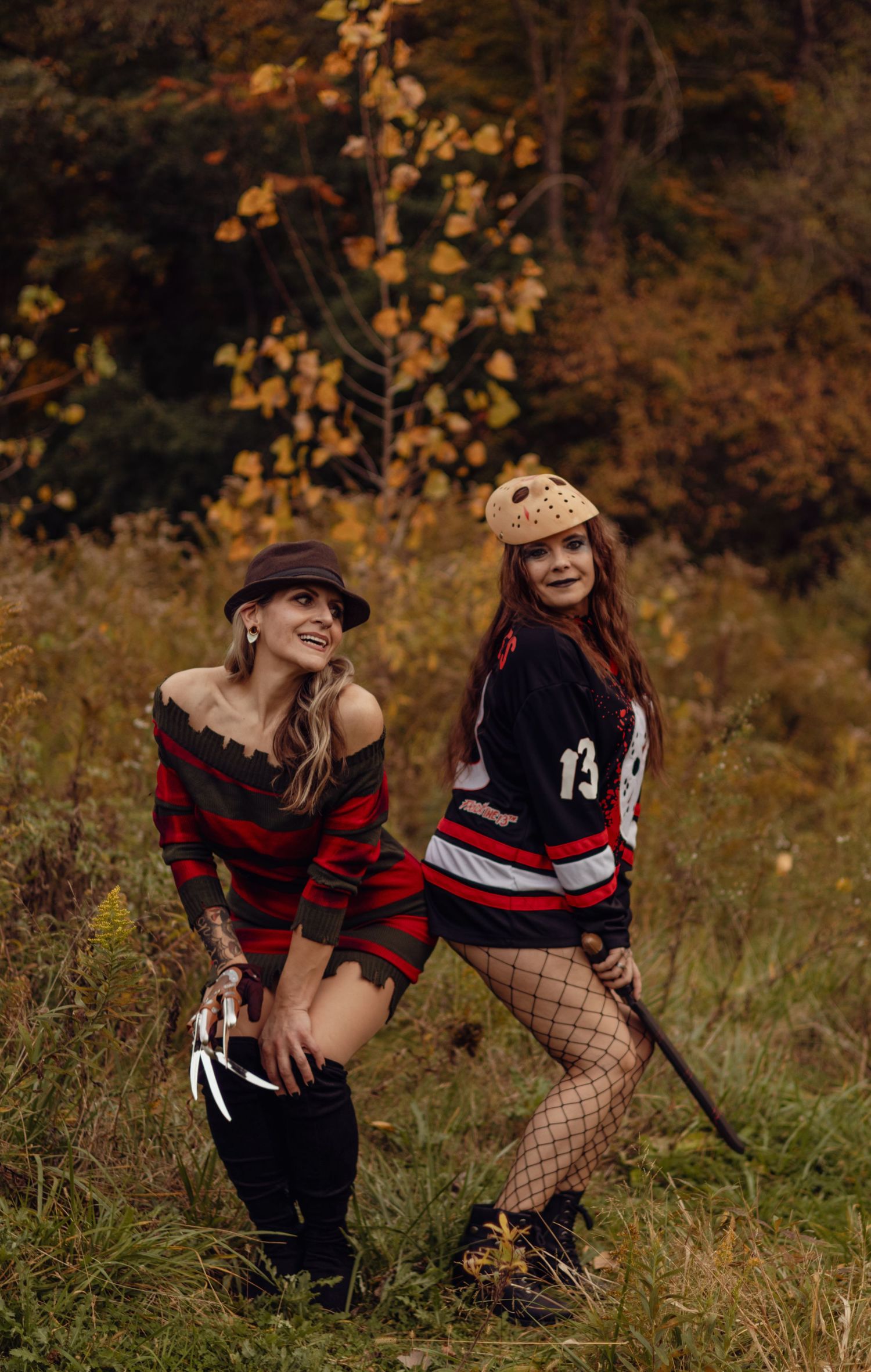 Two women in Freddy Krueger and Jason Voorhees Halloween costumes posing outdoors in autumn foliage.
