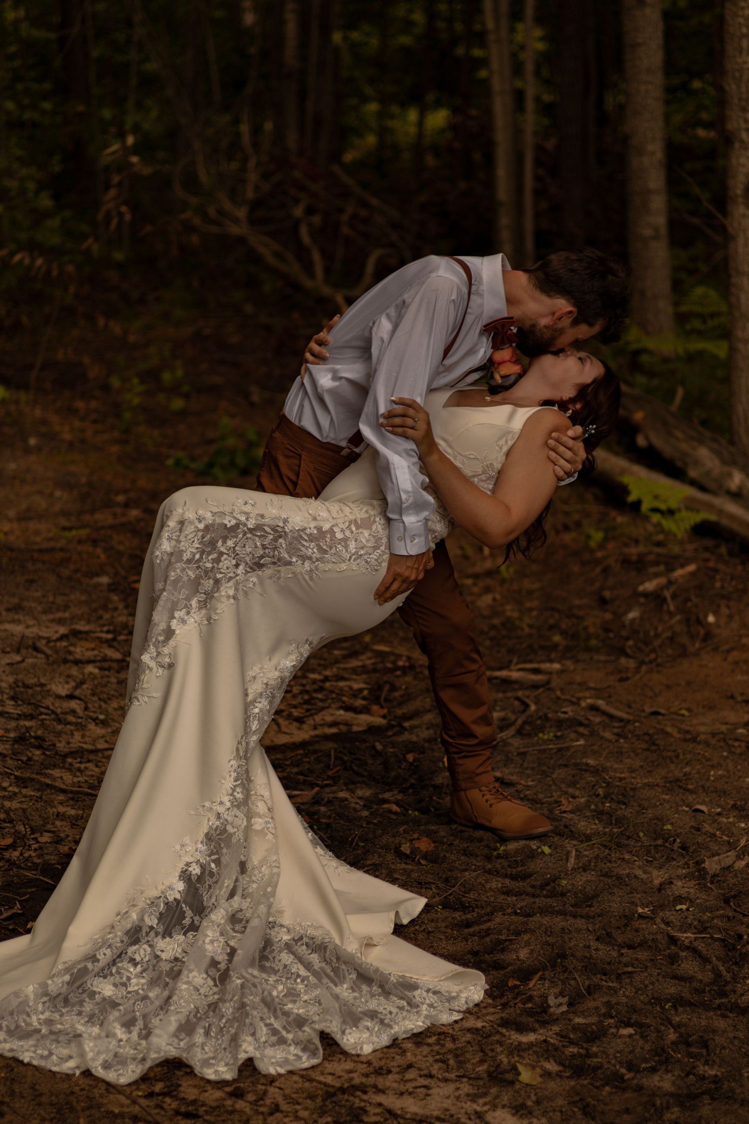 A romantic wedding photo in the forest shows a couple in a dramatic dip pose, with the bride wearing a lace-detailed gown.