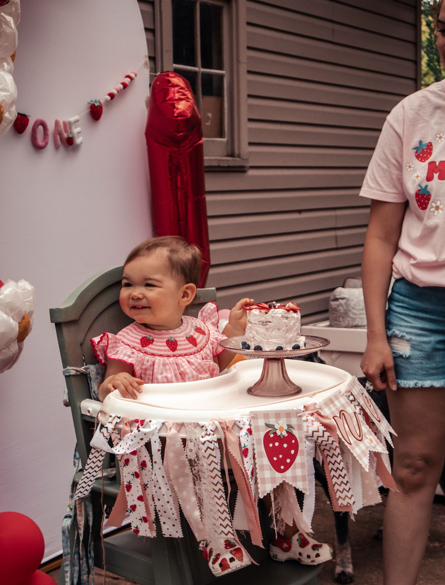 Birthday party setup with high chair decorated in pink and white heart-themed bunting.
