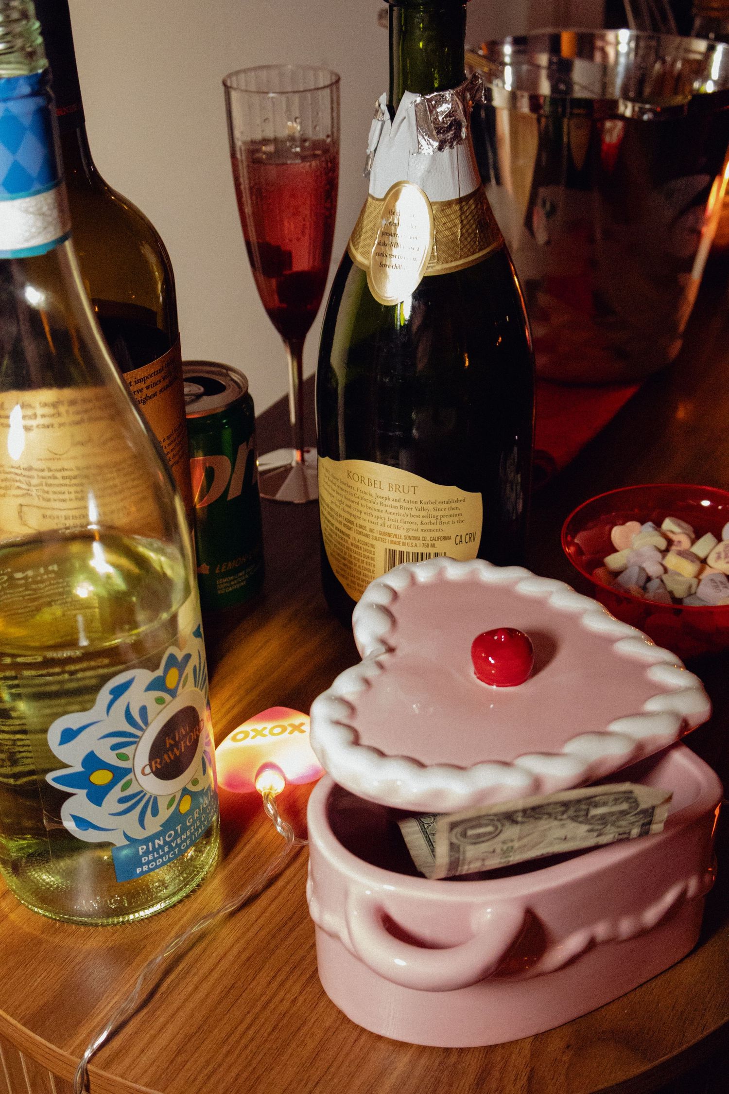 Pink ceramic ashtray with a decorative scalloped edge sits on a wooden table among various bottles and glassware.
