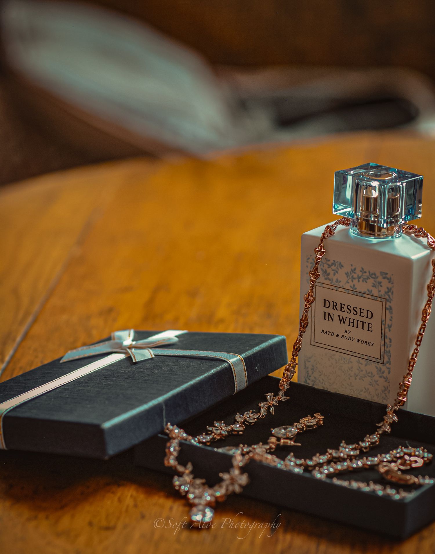 Silver perfume bottles and delicate pearl necklaces arranged on a wooden surface in warm lighting.