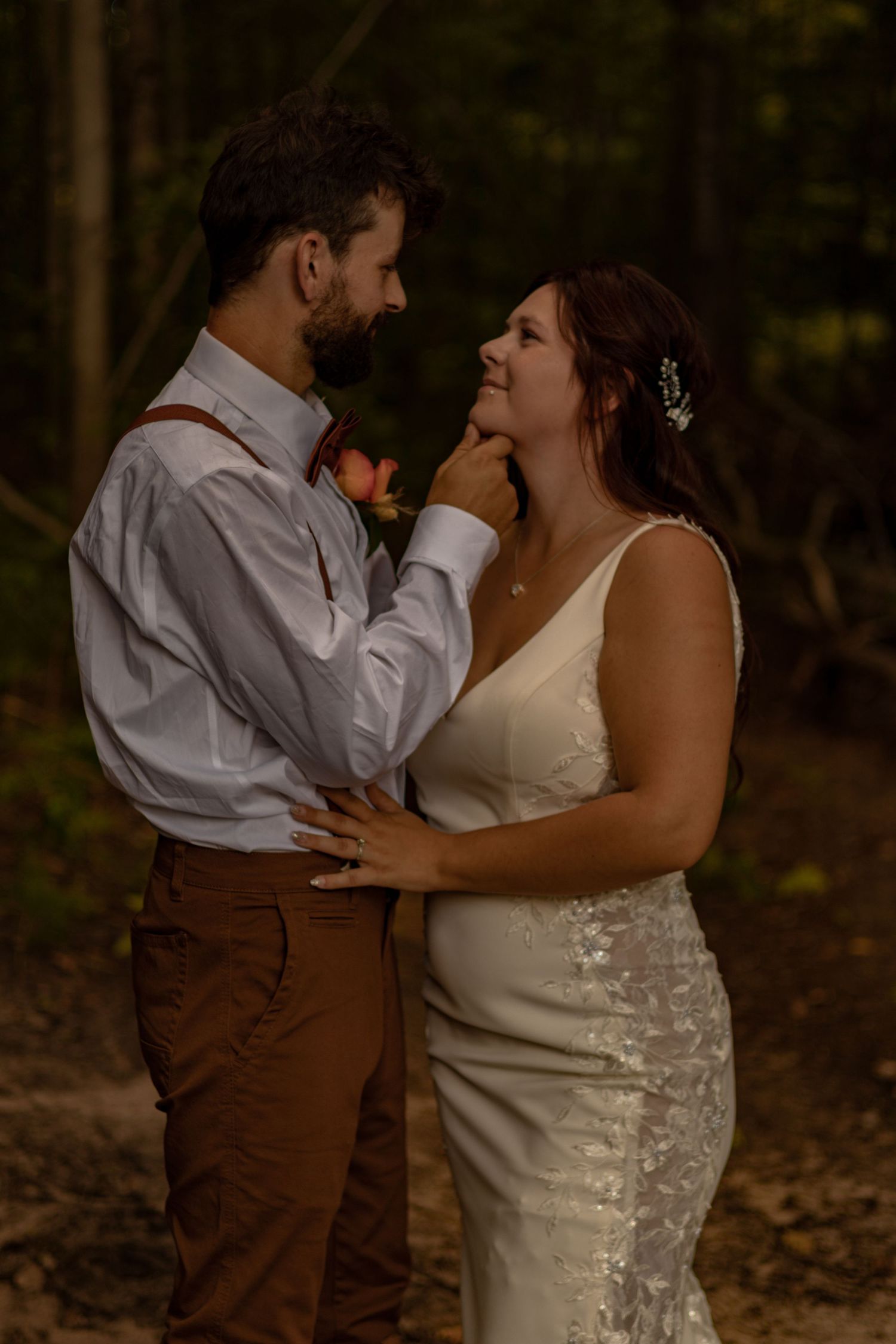 A romantic wedding couple shares an intimate moment in a wooded setting during golden hour.