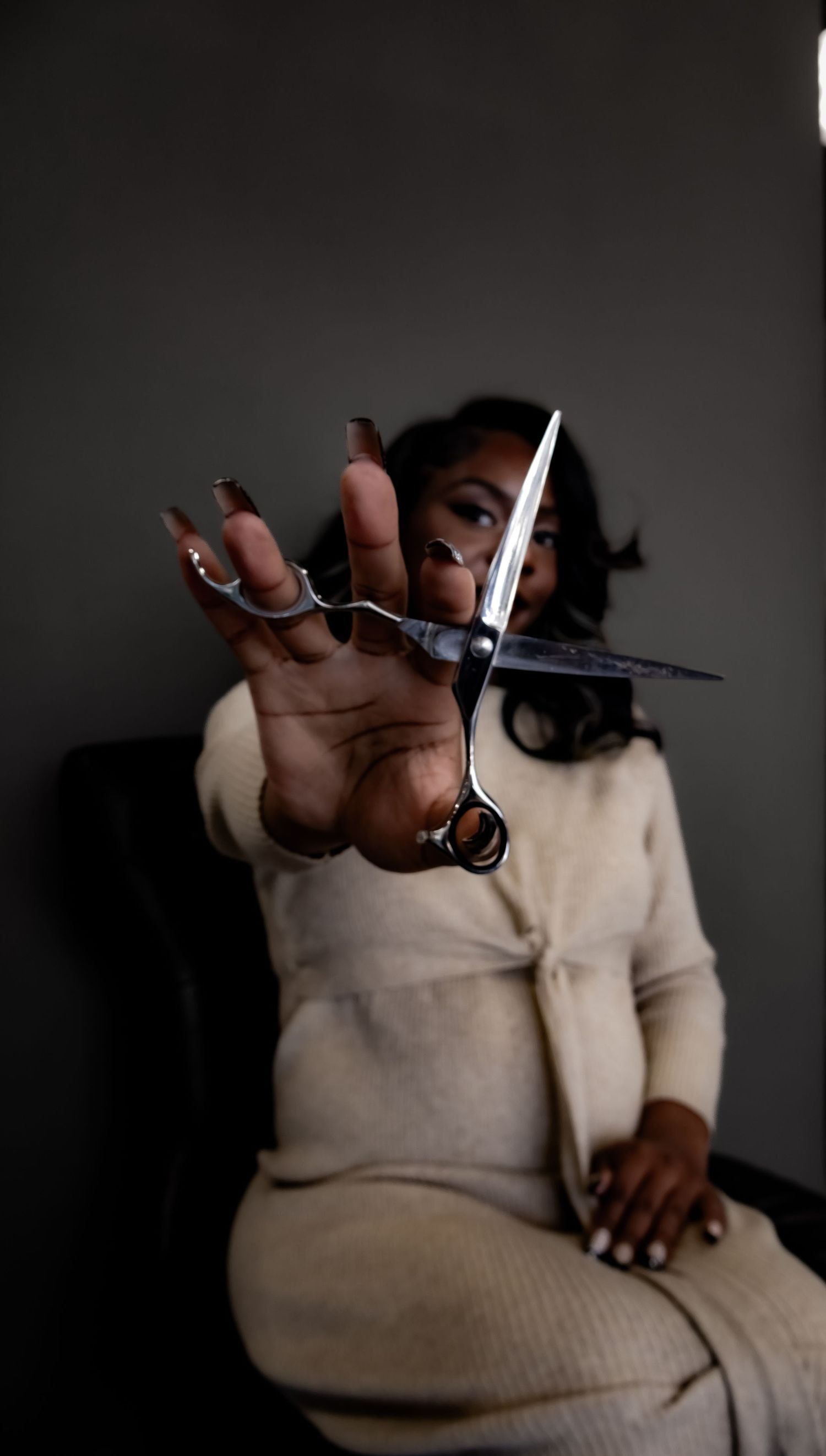 Dramatic low-light photography featuring hands demonstrating hairdressing scissors against dark backdrop.