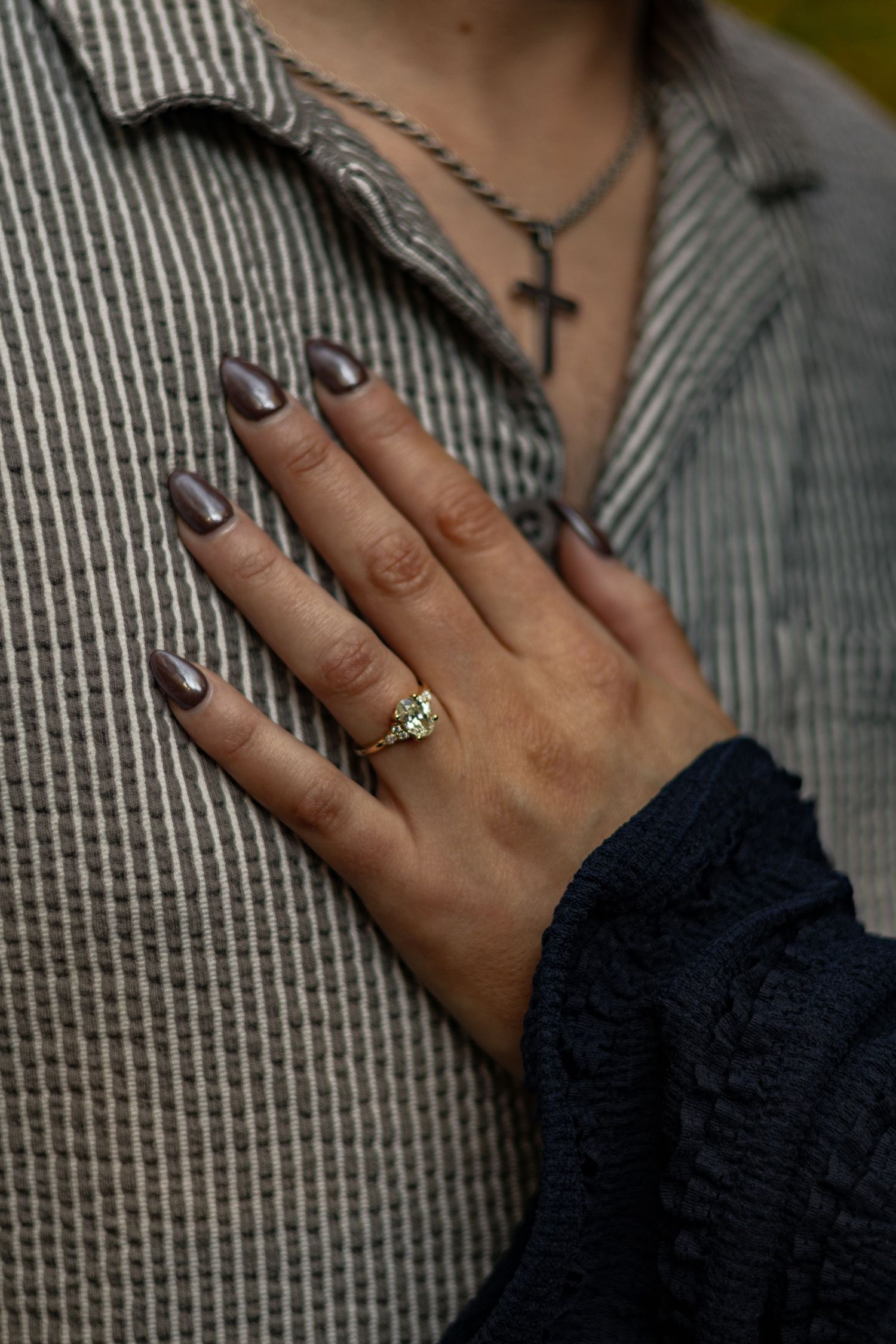 Close-up of a hand wearing a ring and dark nail polish against a striped fabric background.