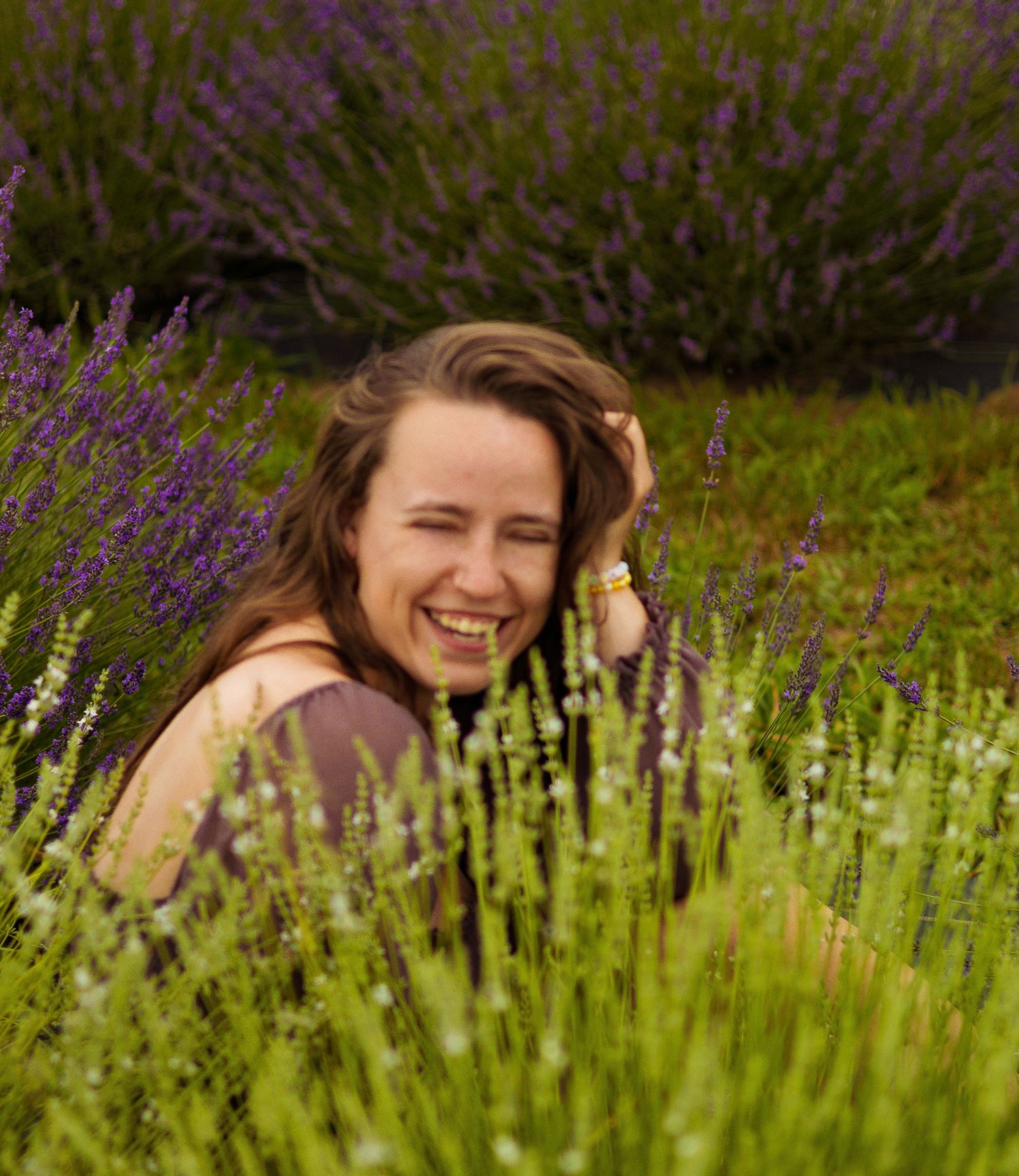 Someone playfully peeks through purple lavender flowers in a sunny garden field.