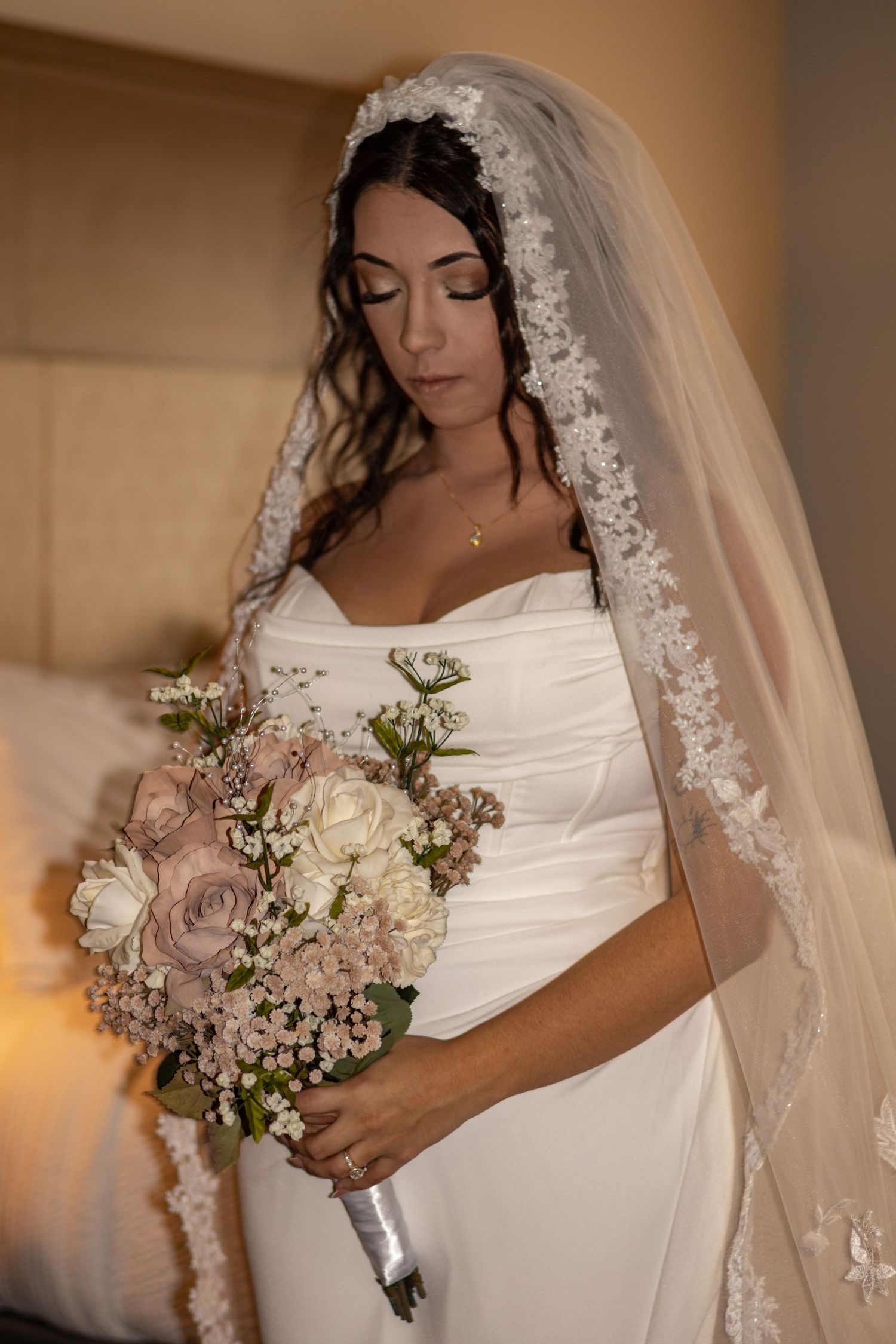 A bridal portrait showing an elegant white dress and lace-trimmed veil with a soft pink bouquet.