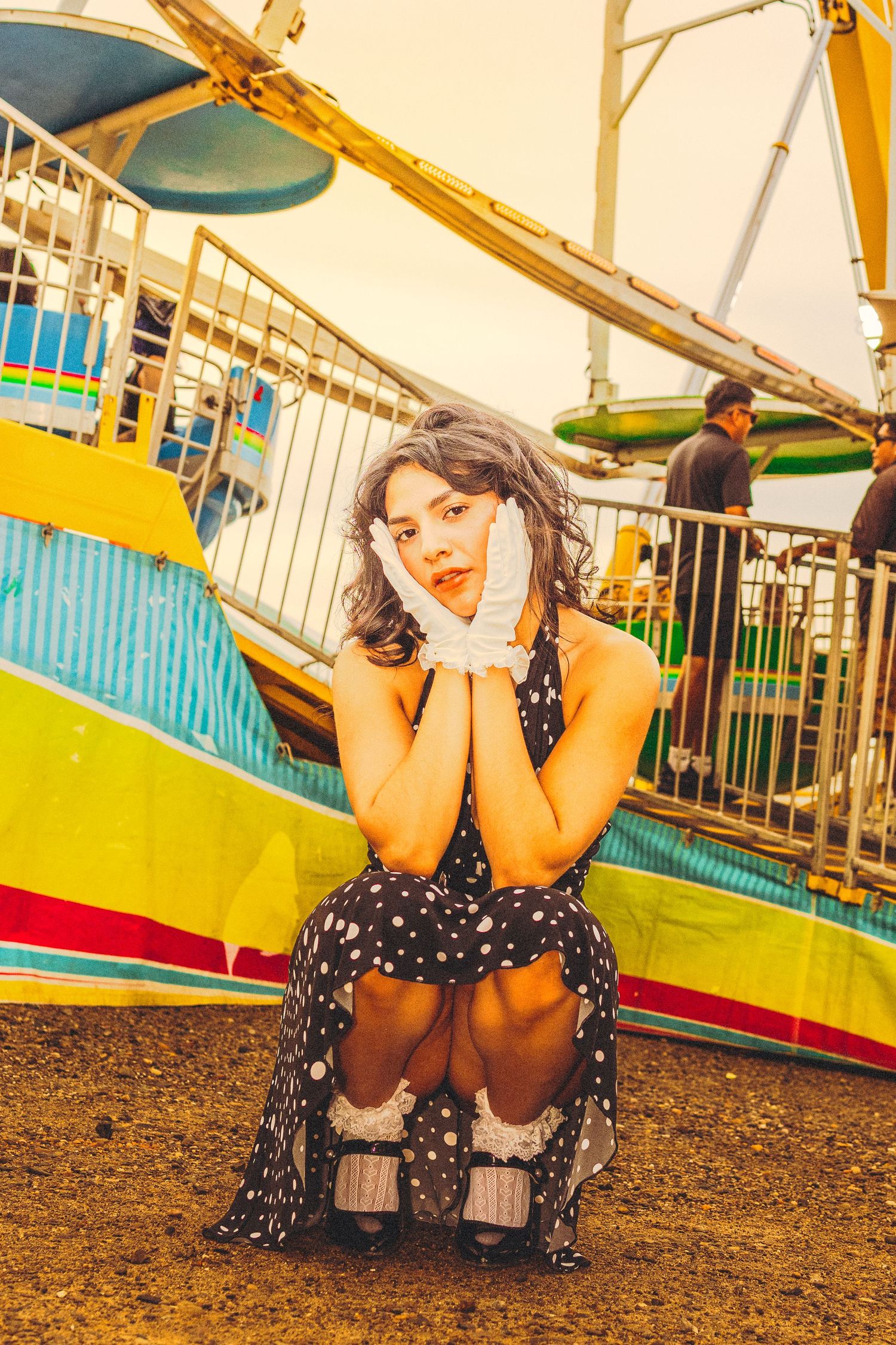 Young woman in polka dot dress sitting at amusement park with Ferris wheel in background.