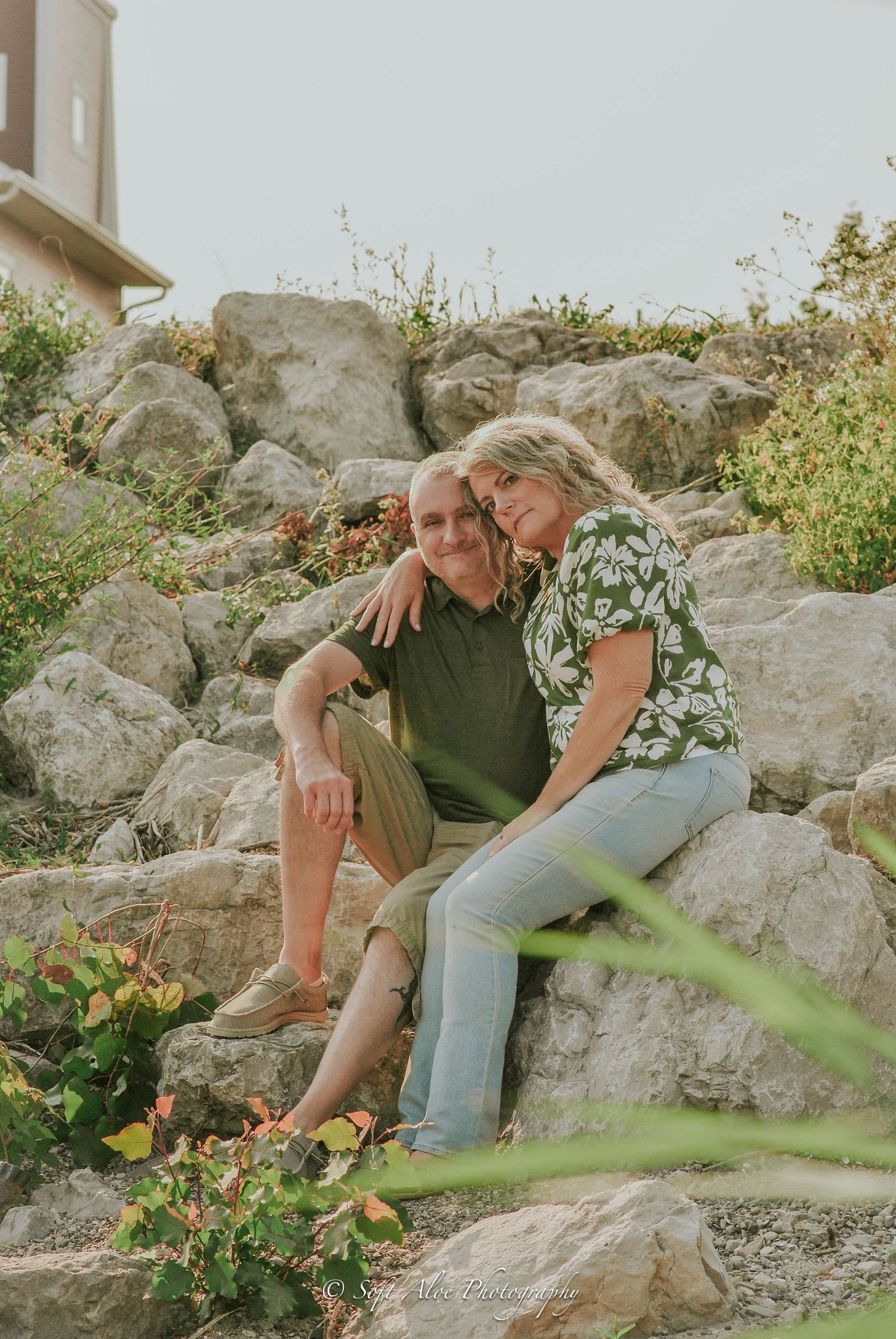 A romantic couple sharing a tender moment on rocky terrain surrounded by greenery.