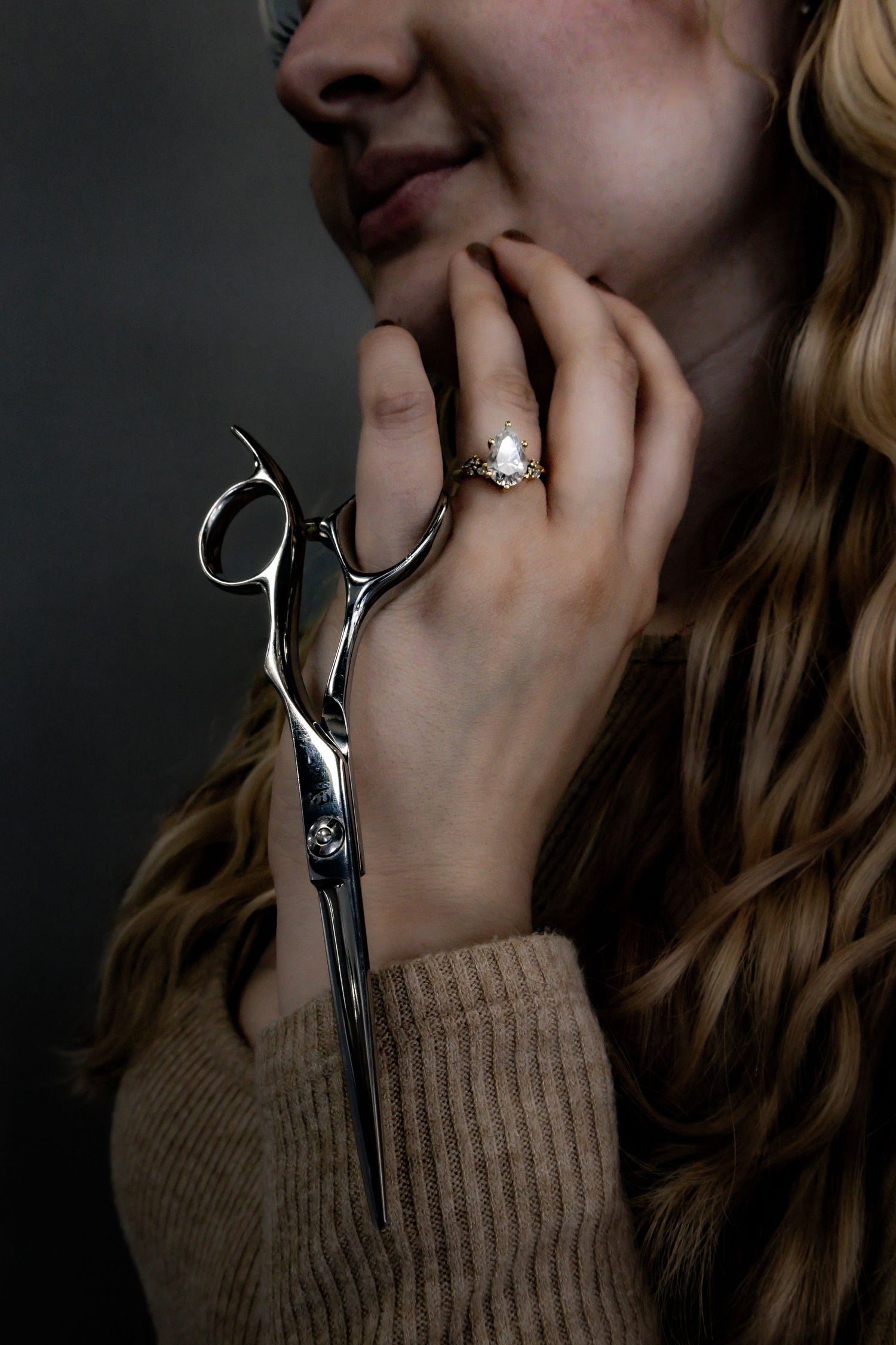 Close-up shots of silver hairdressing scissors held against a beige sweater sleeve.