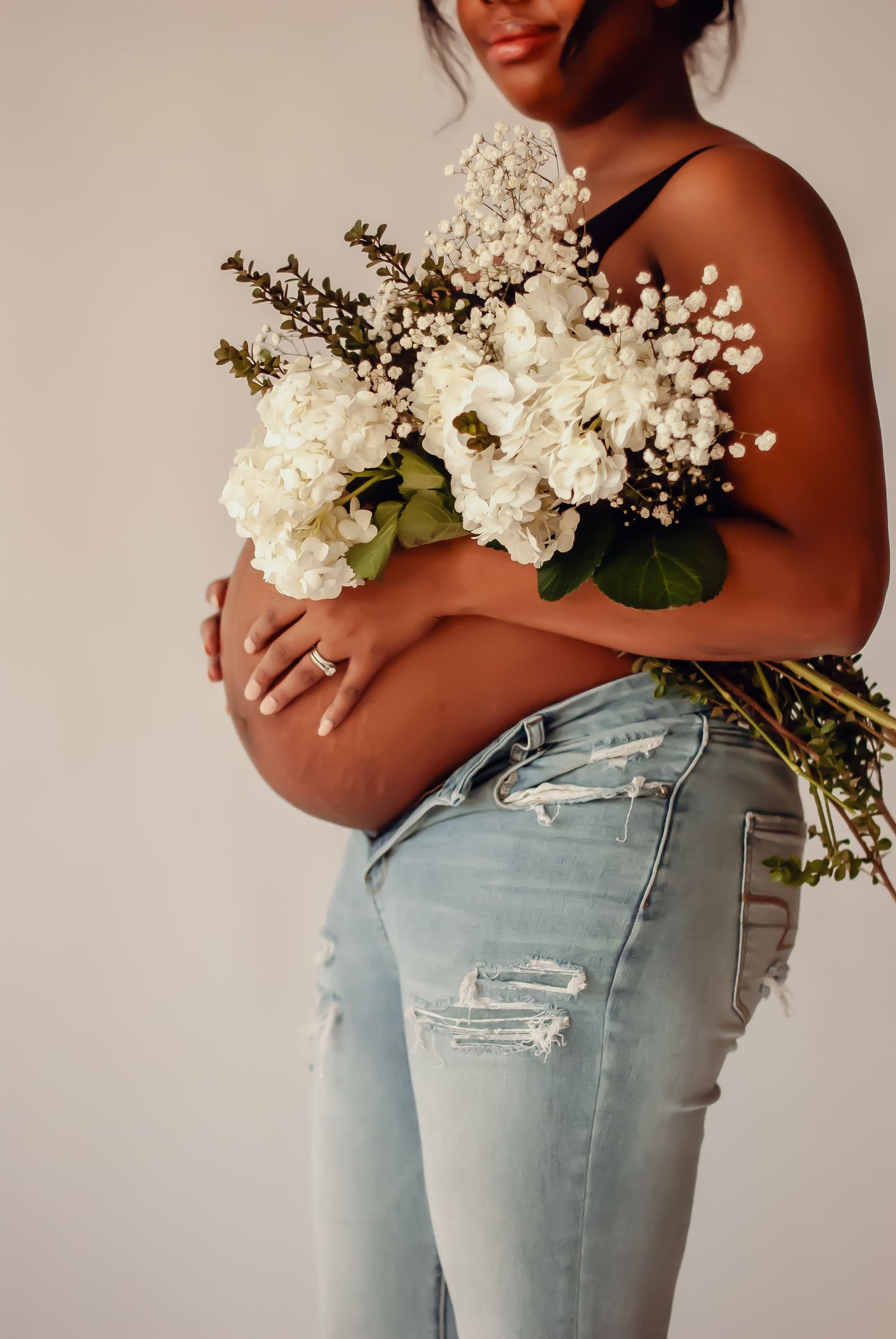 Person wearing light blue distressed denim jeans holds delicate white floral bouquet against neutral background.