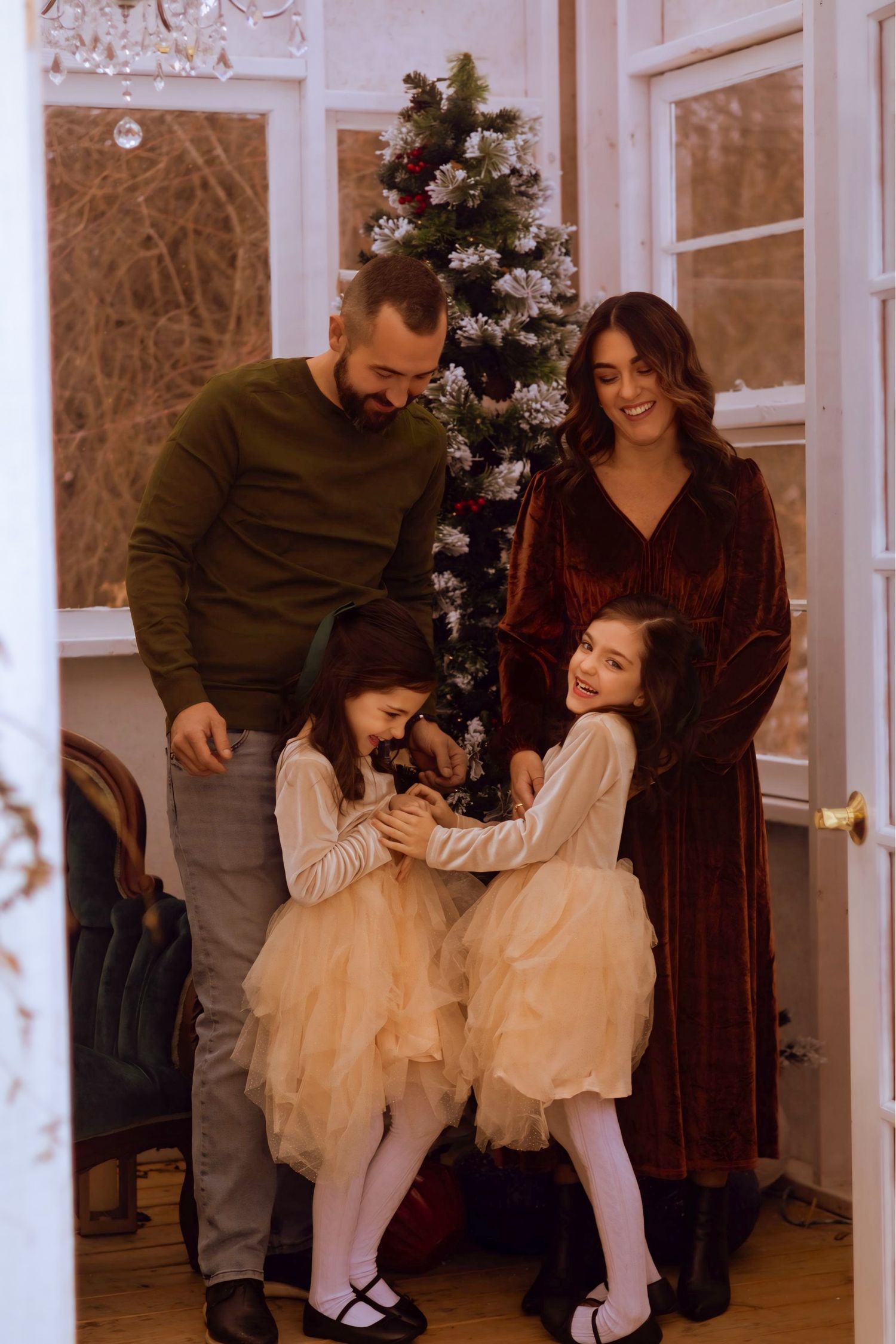 Family shares joyful moments dancing together in a living room decorated for Christmas with a tree in the background.