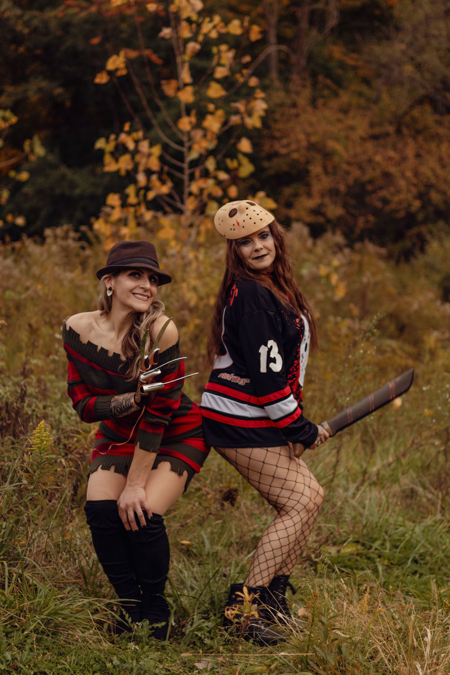 Two people in Halloween costumes with red and black outfits pose playfully in an autumn field with fall foliage.