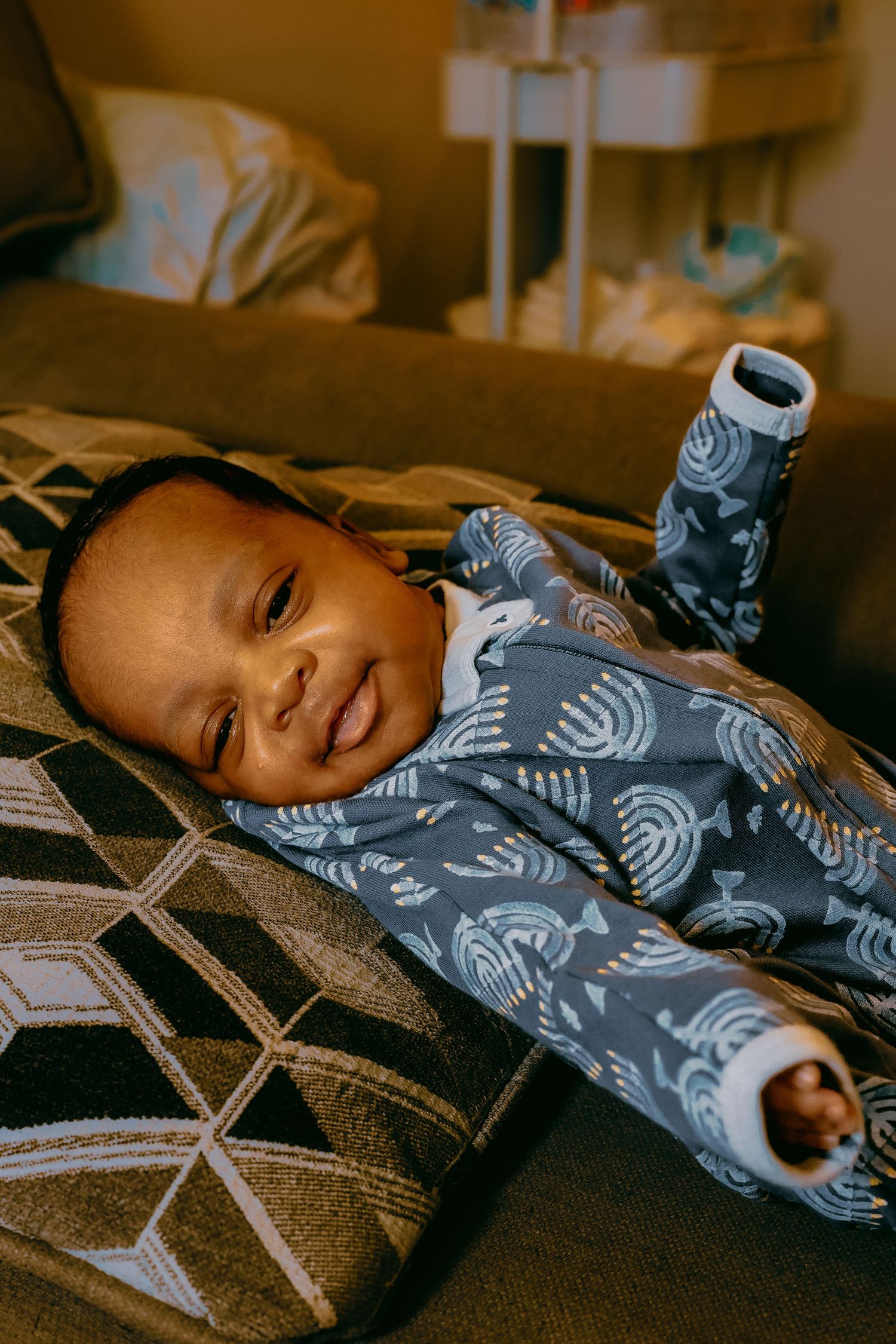 Smiling baby in blue whale print pajamas lying on a couch cushion in a cozy room.