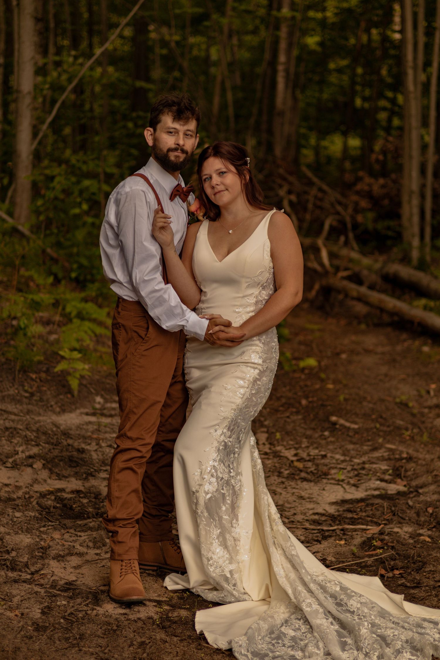 A couple shares a romantic moment in a forest setting, with the bride wearing a flowing lace wedding gown.