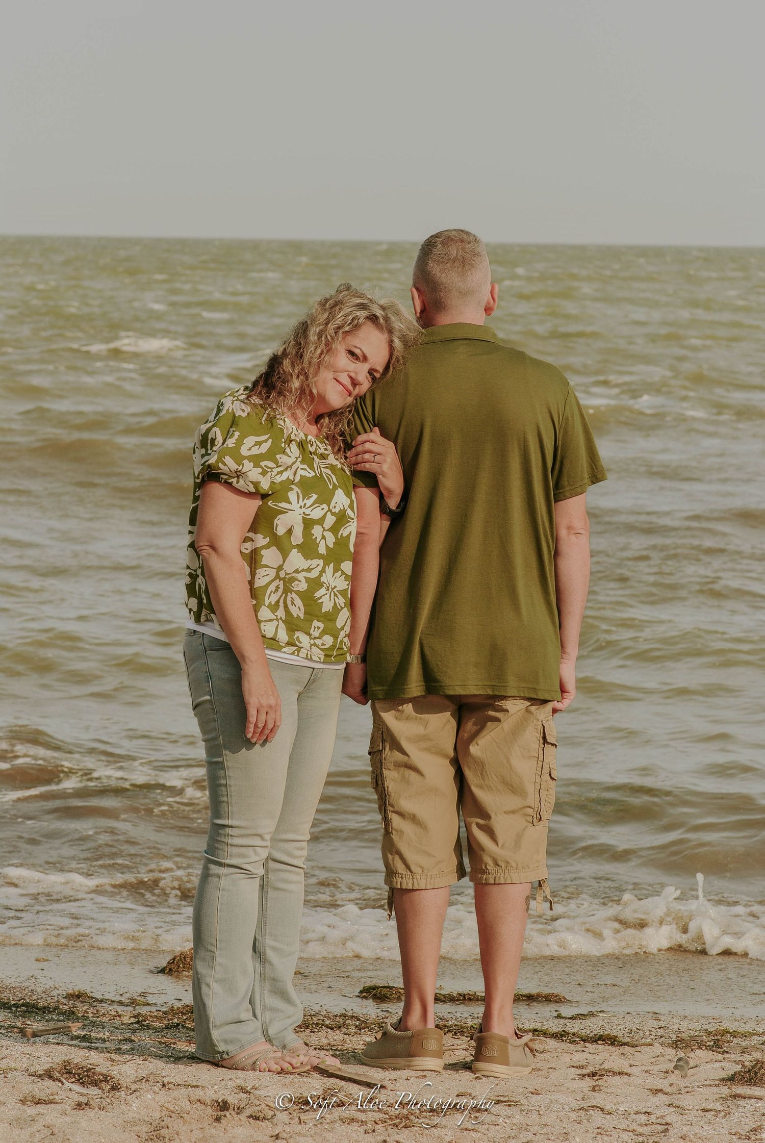 Couple walking together on a sandy beach at sunset with waves in the background.