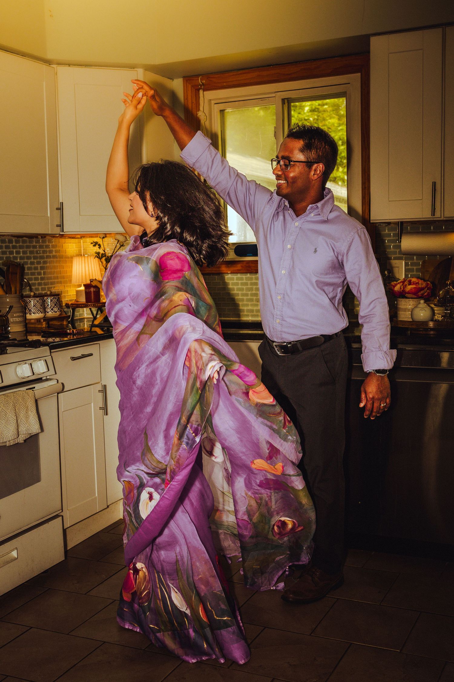 Couple dancing in kitchen, woman in colorful purple sari, man in blue shirt, spinning gracefully.