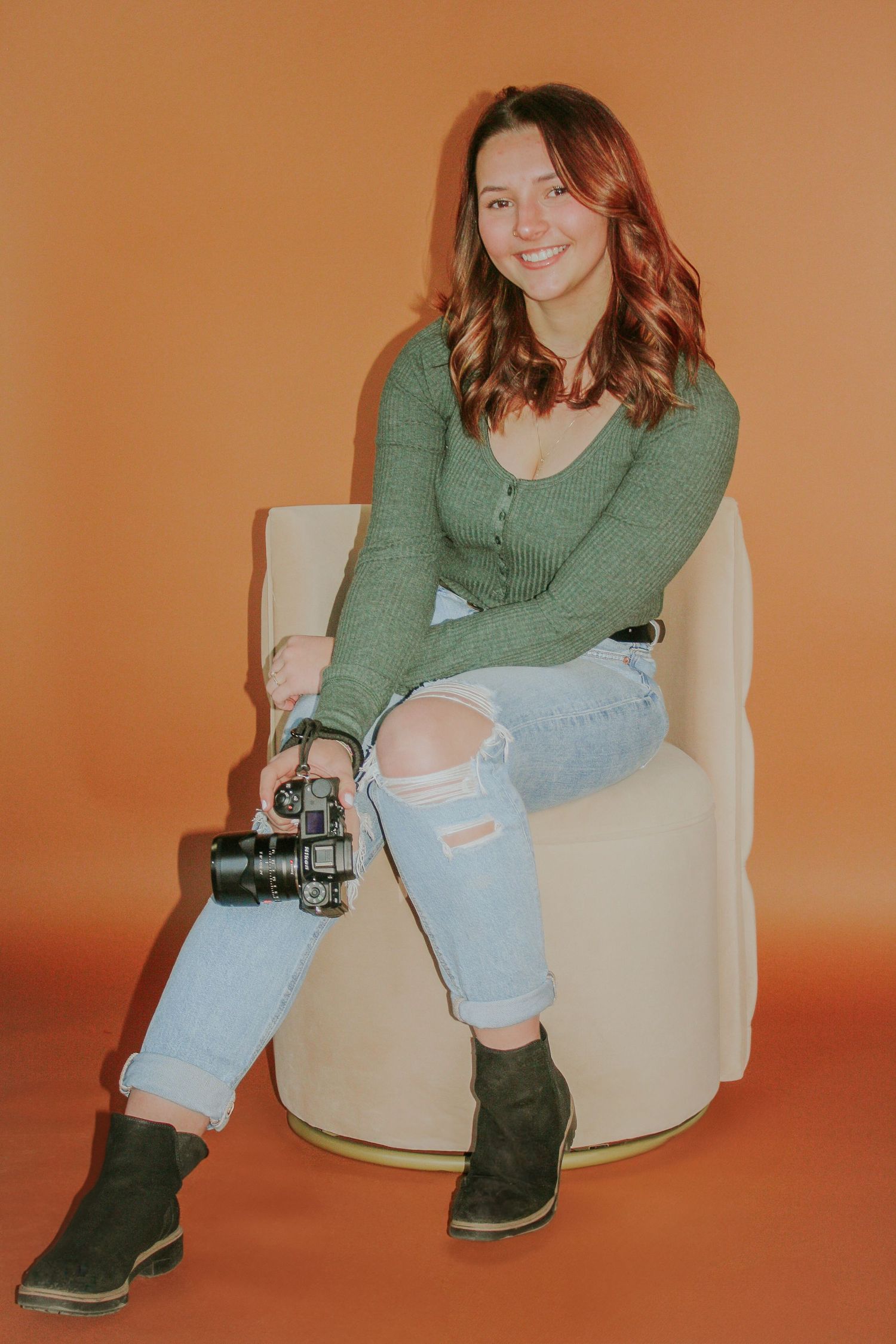 Casual photoshoot featuring green sweater and ripped jeans in a studio with orange backdrop.