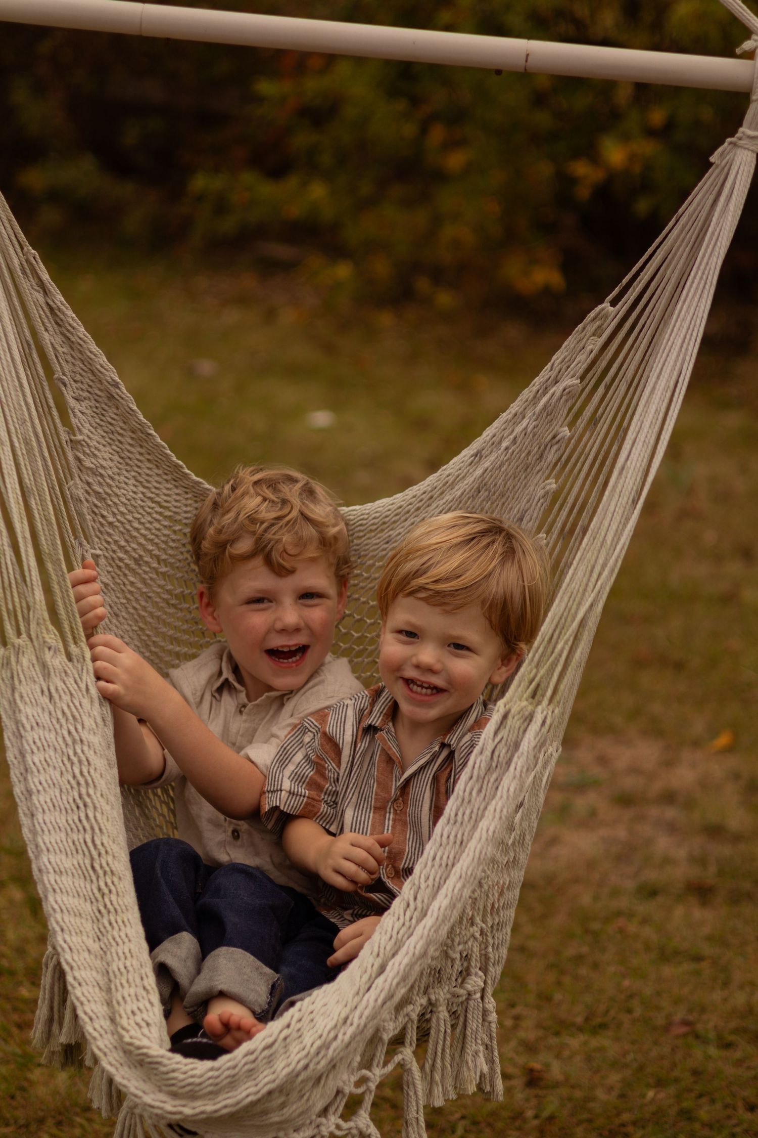Two children laugh while sitting together in a macrame hammock.