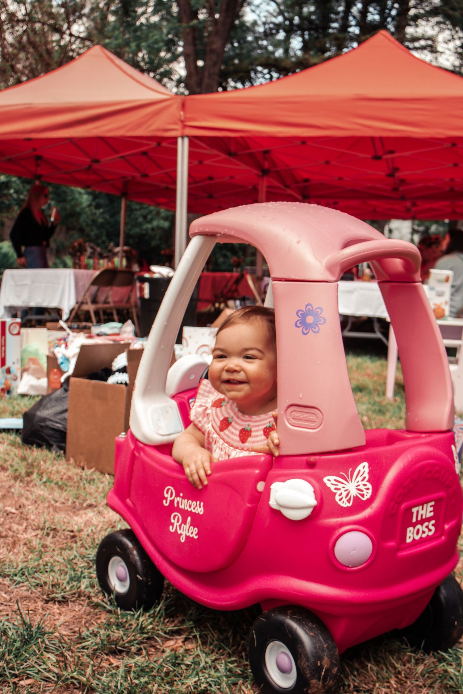 Pink toy cars lined up outdoors under red canopy tents.