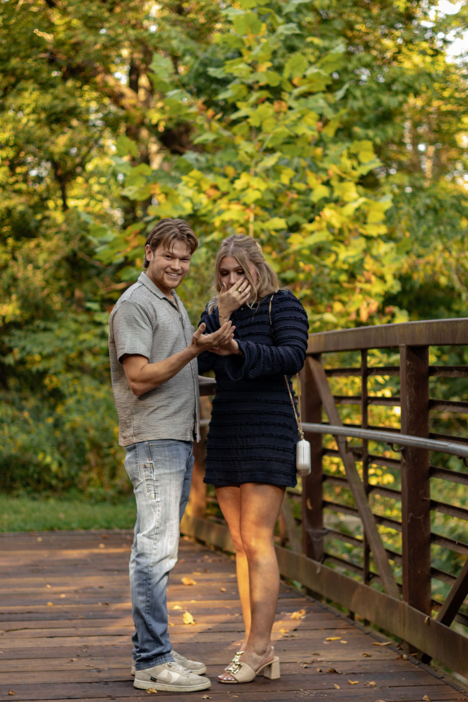 Emotional reaction captured during a proposal on a wooden bridge surrounded by fall trees.