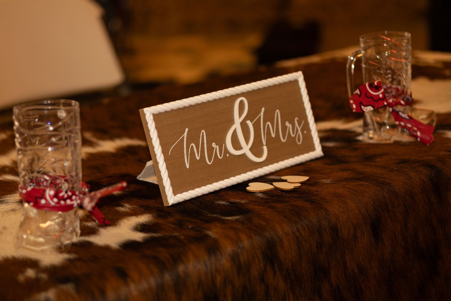 Mr. & Mrs. sign on a rustic cowhide table runner at a wedding reception with glasses and ribbon decor.