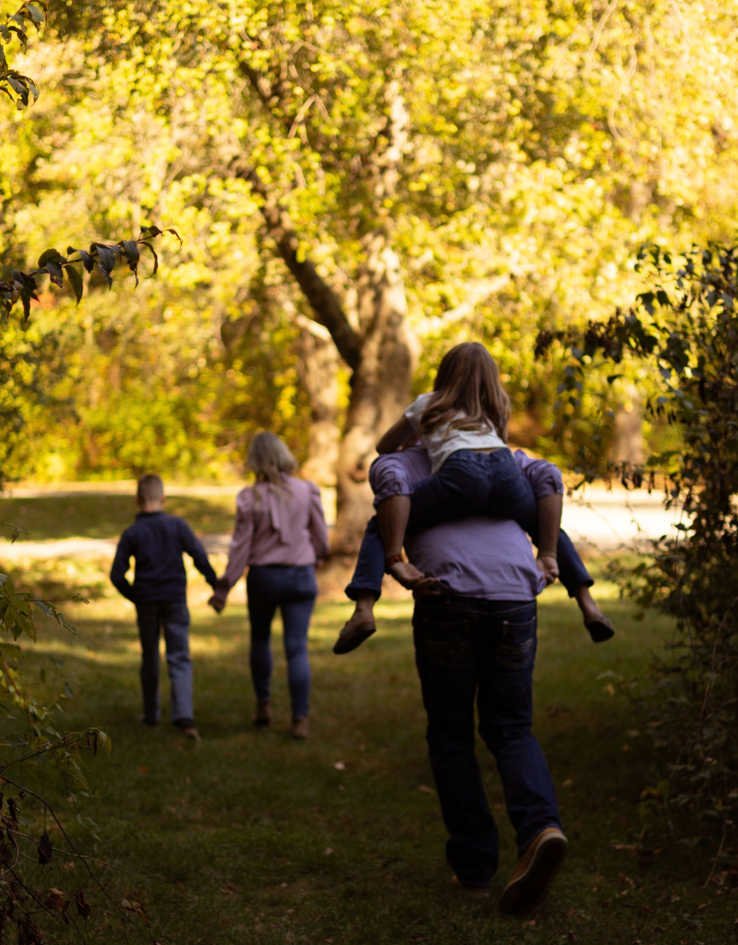 Family walking together on an autumn path with golden trees and sunlight filtering through the branches.