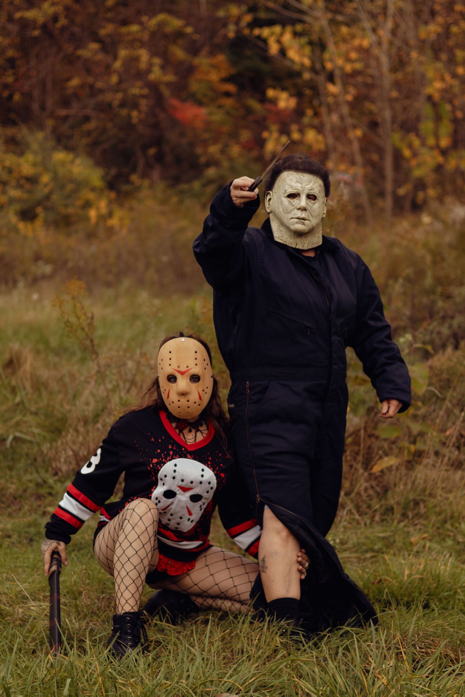 Two people in Halloween costumes as Jason Voorhees and Michael Myers posing outdoors in autumn setting.