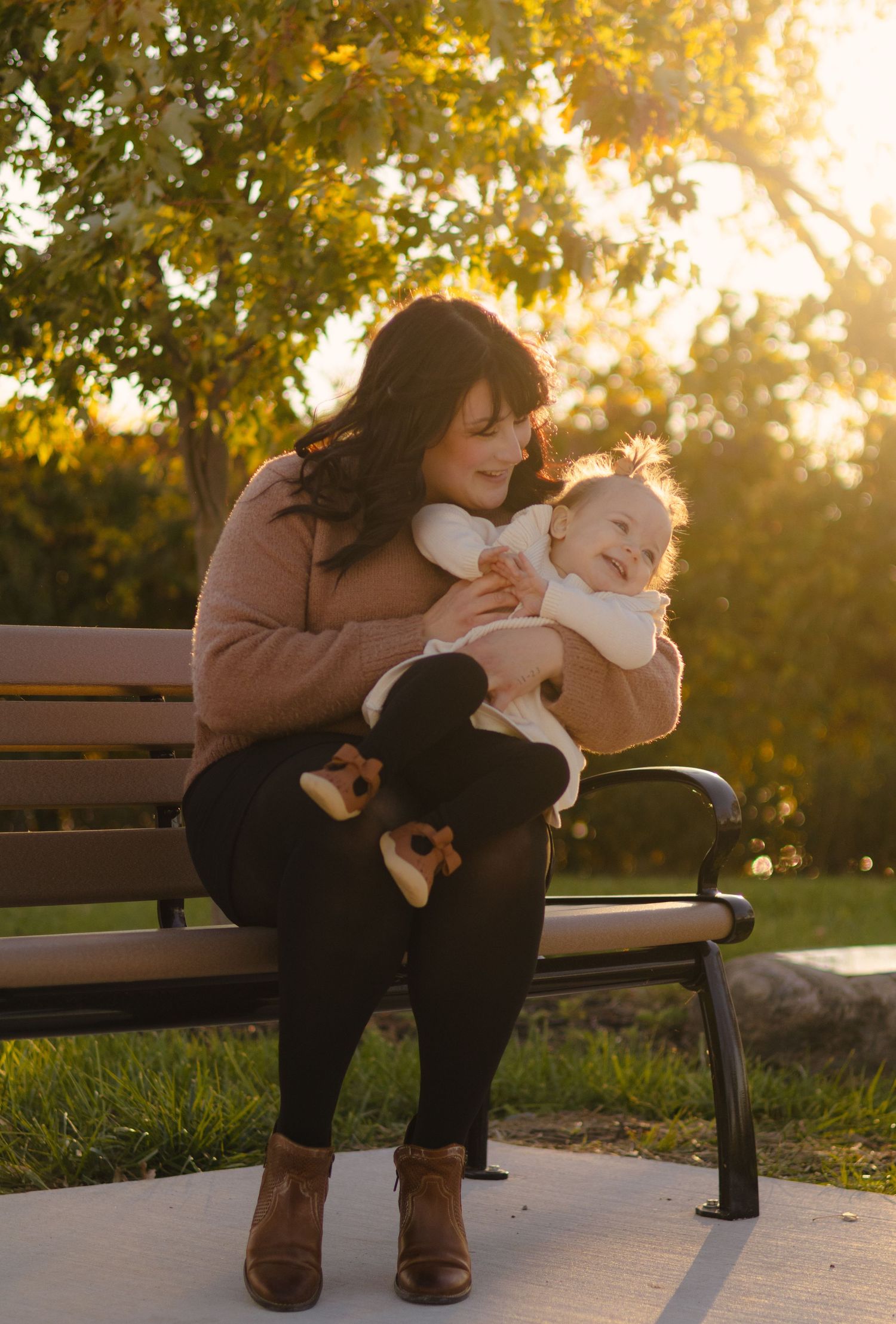 Person sitting on a park bench at sunset holding a small white dog.
