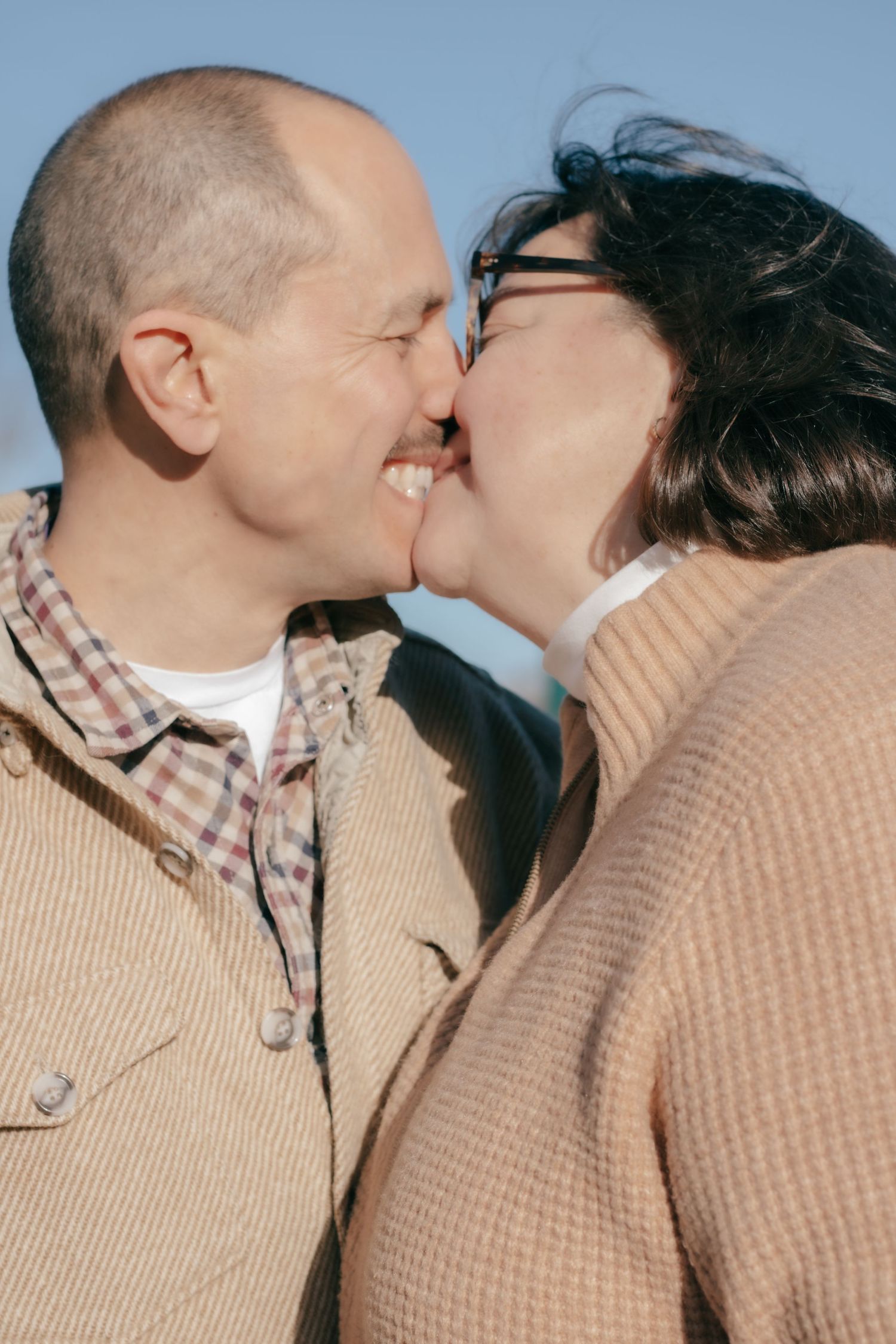 Two people in casual sweaters share an intimate moment against a neutral background.