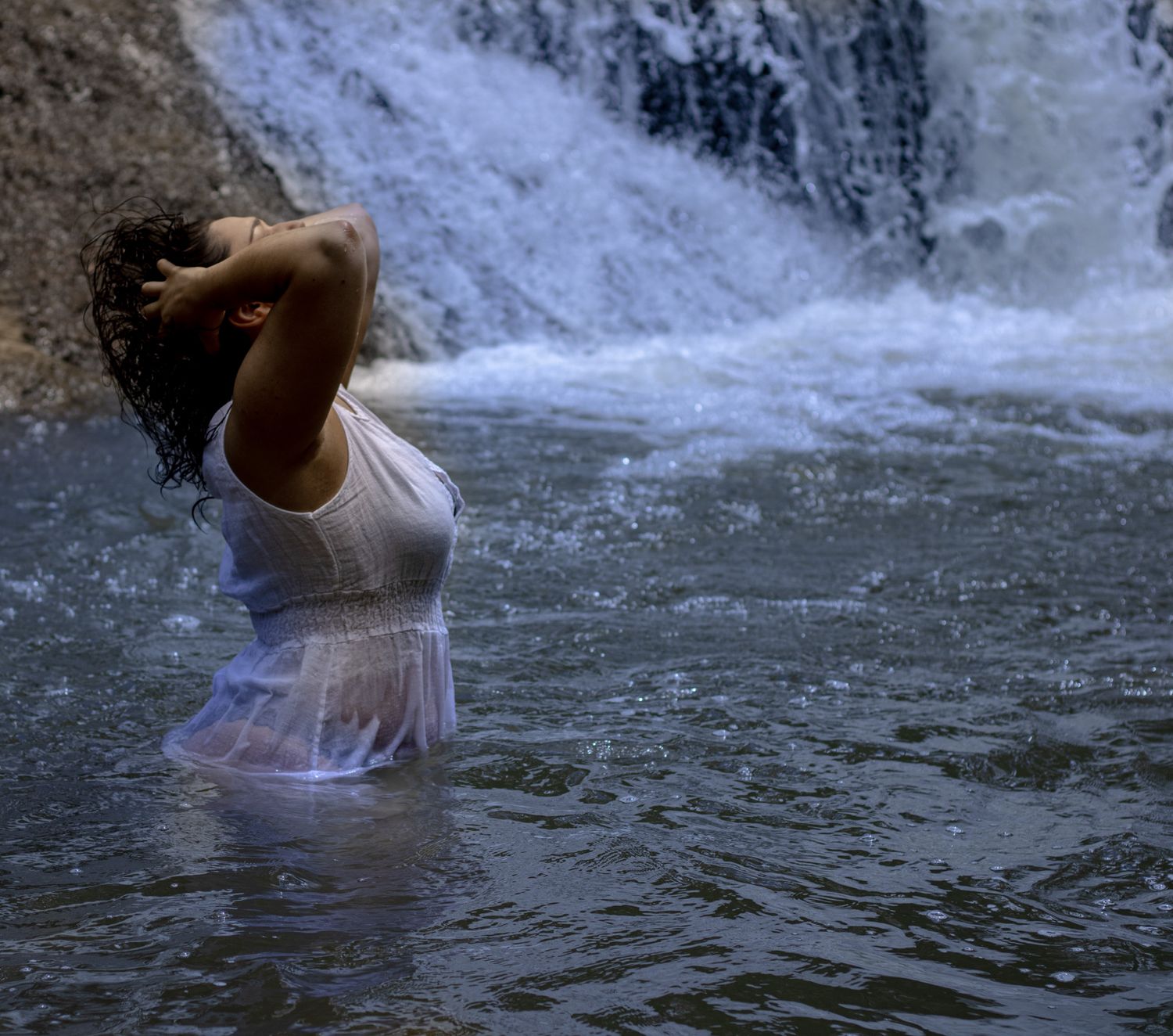 Figure in white dress standing in waterfall spray with dramatic lighting.