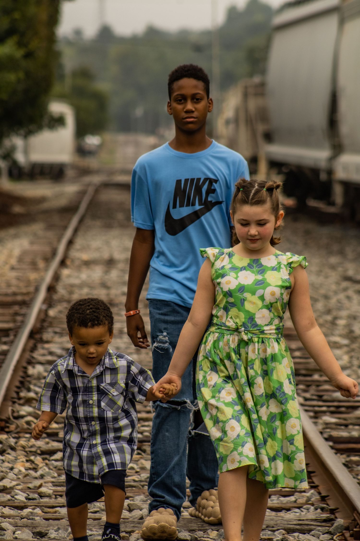 Three people walking along railroad tracks wearing casual summer outfits.