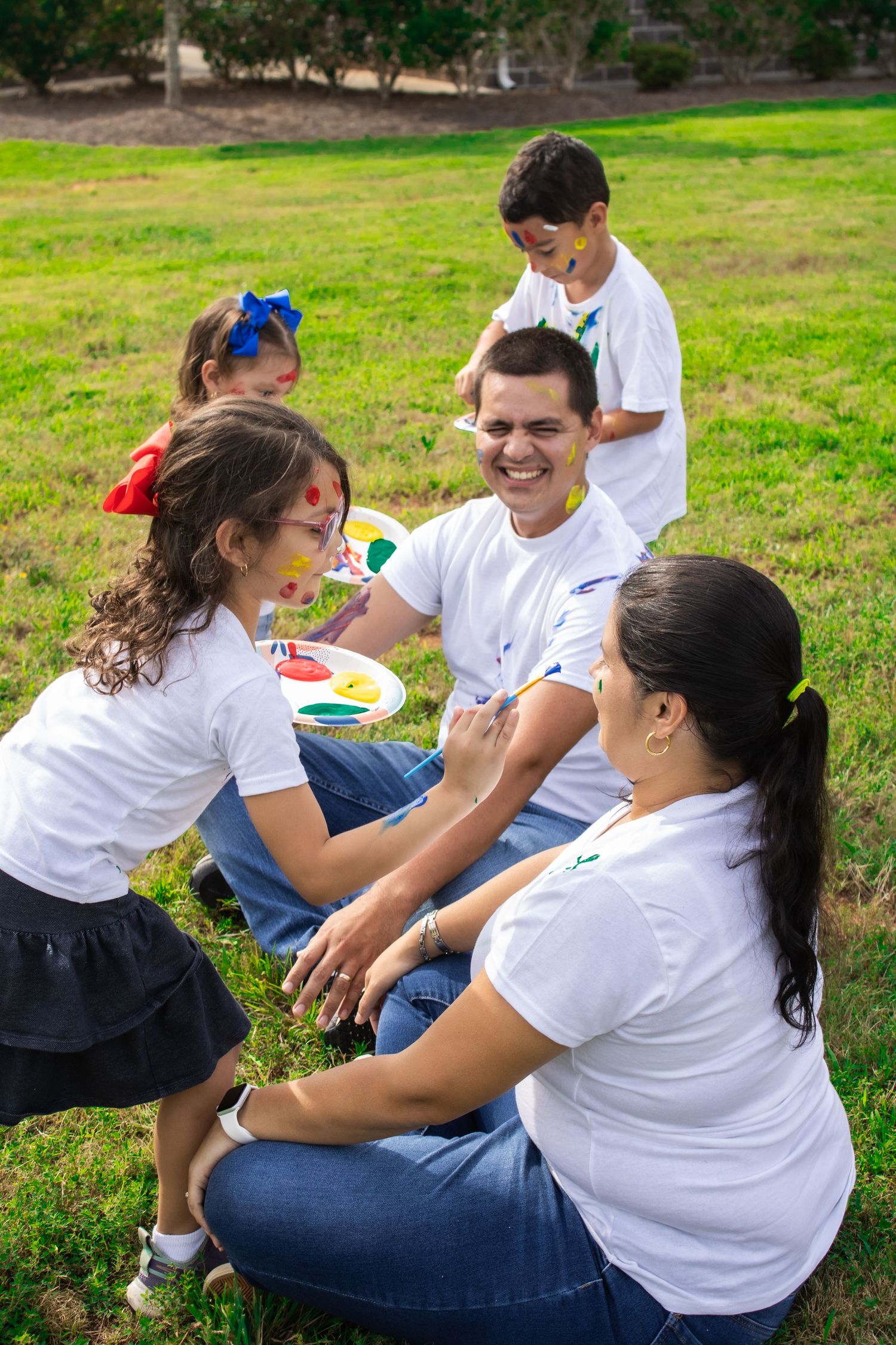 Group members in white shirts play and laugh while sitting on grass.
