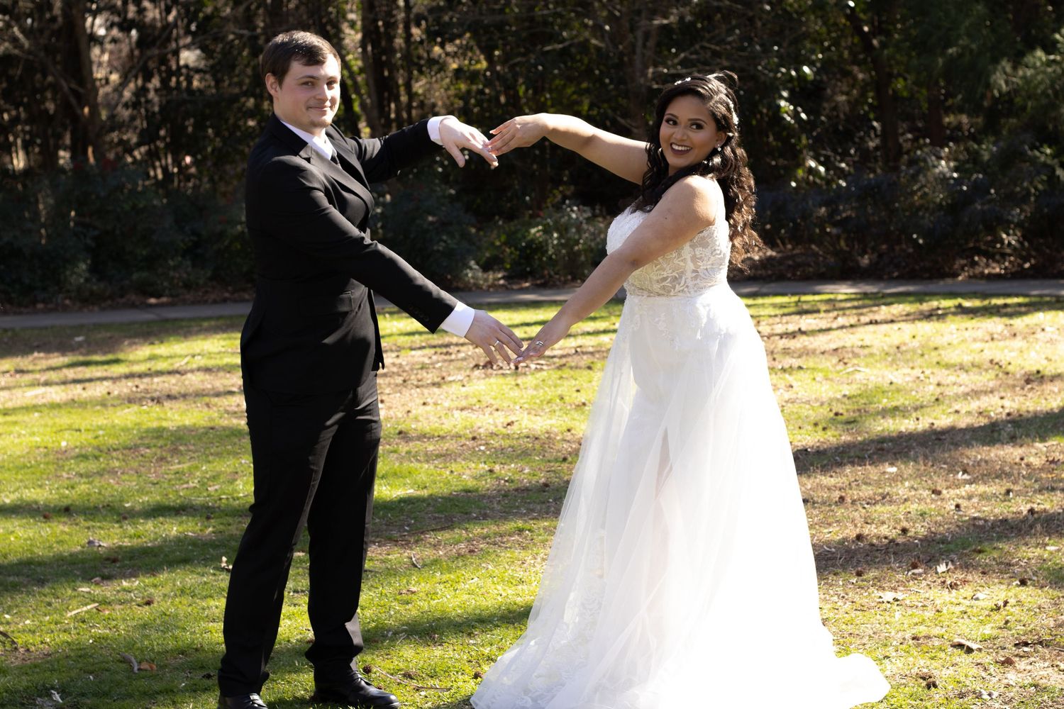 Playful wedding couple dancing and twirling in an outdoor garden setting.